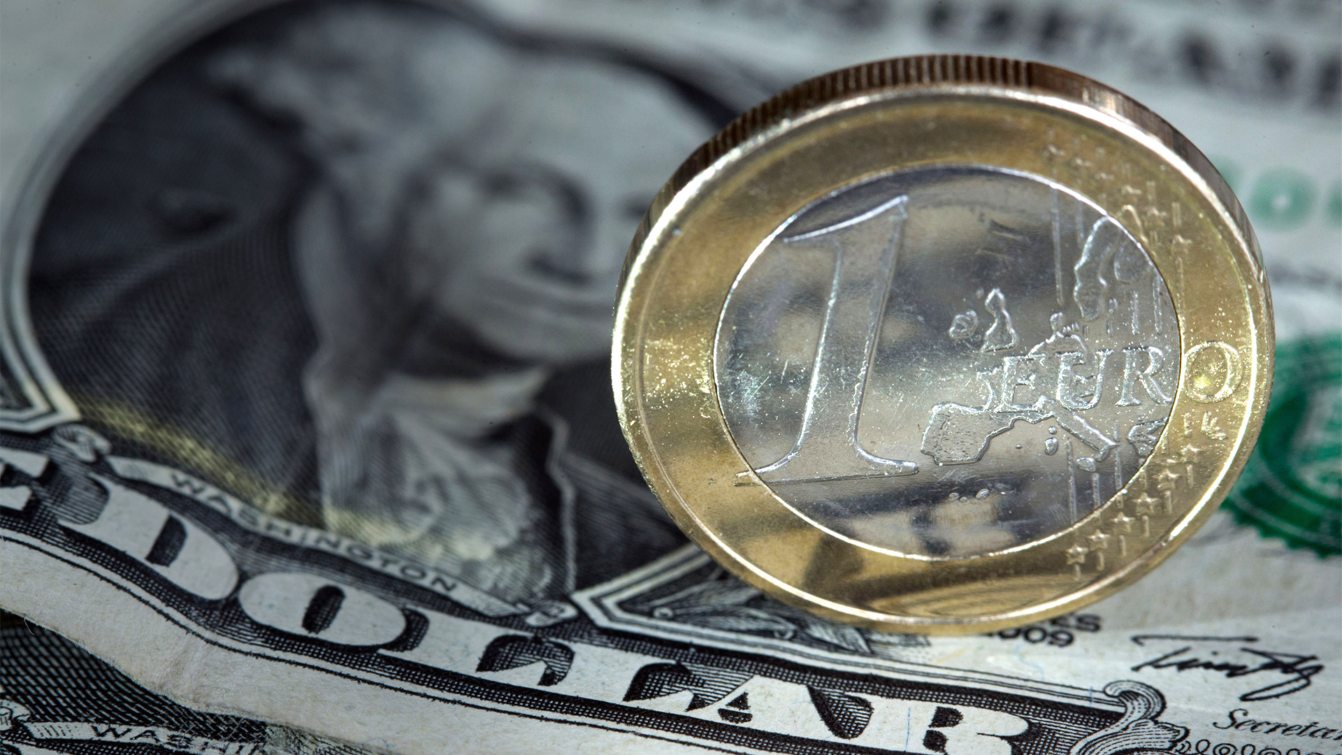 Eine Ein-Euro-Münze steht auf einem Ein-Dollar-Schein