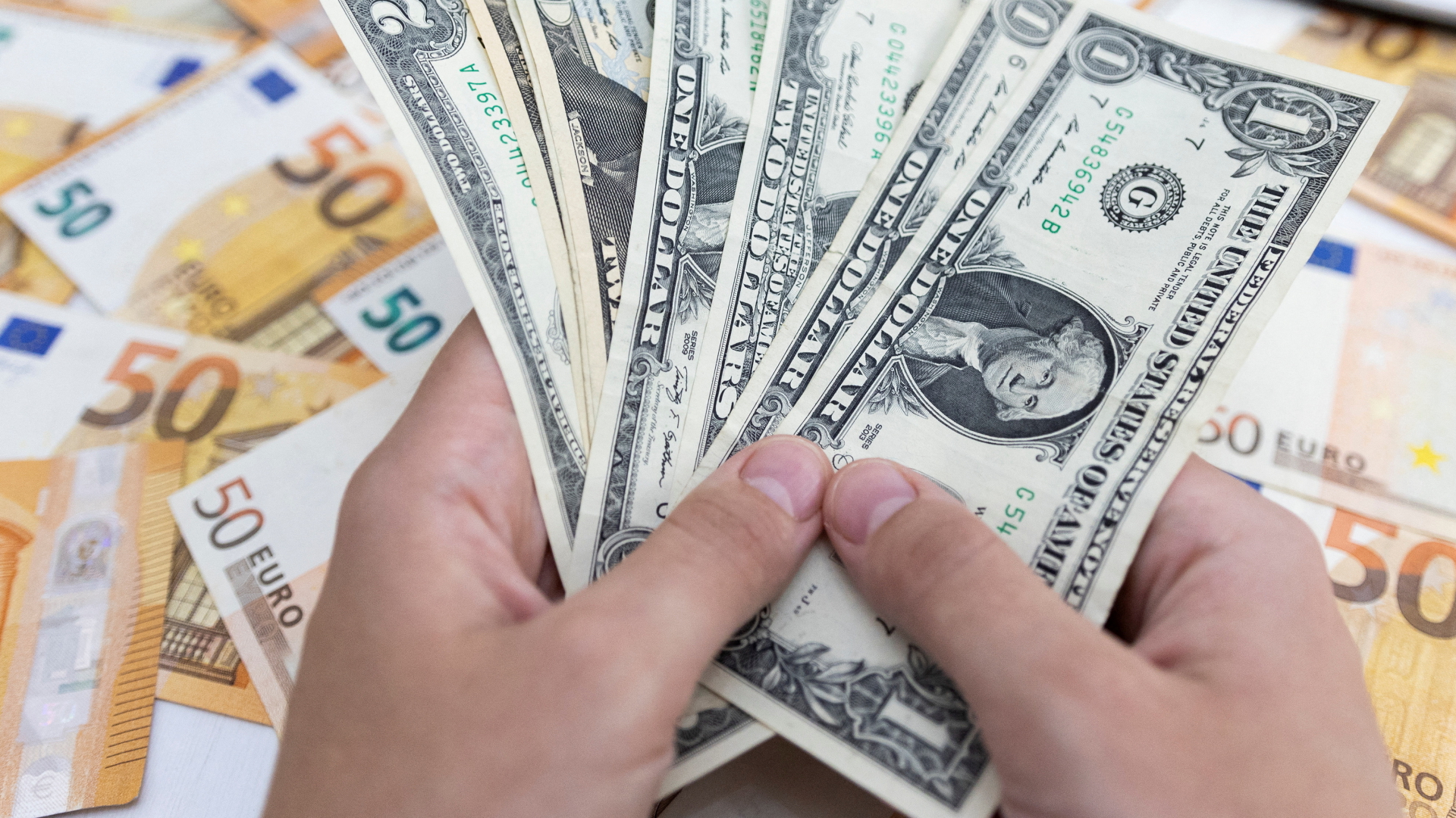 Hand hält Dollar-Scheine über 50-Euro-Scheine | REUTERS