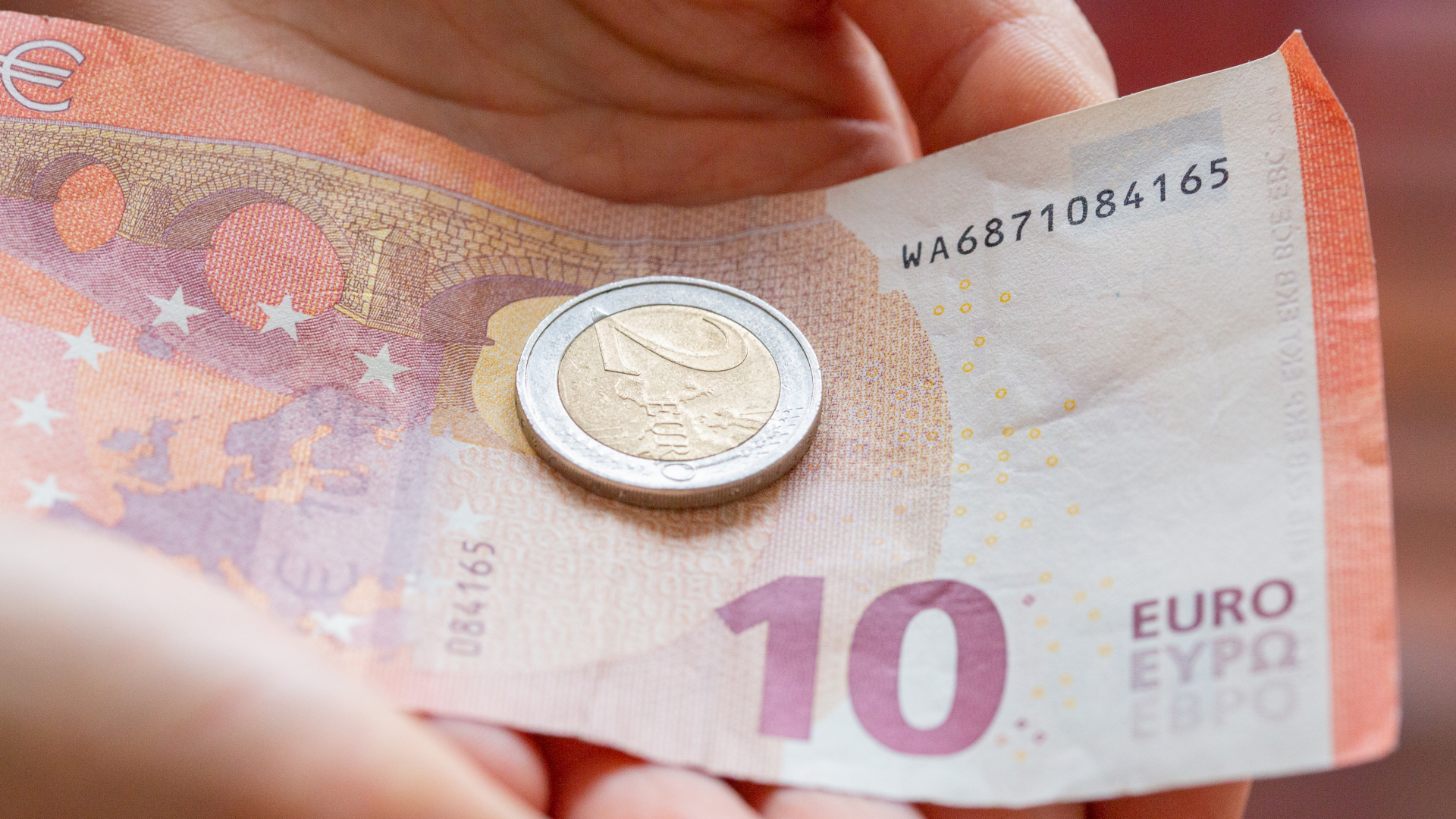 Hände halten einen 10-Euro-Schein und eine 2-Euro-Münze