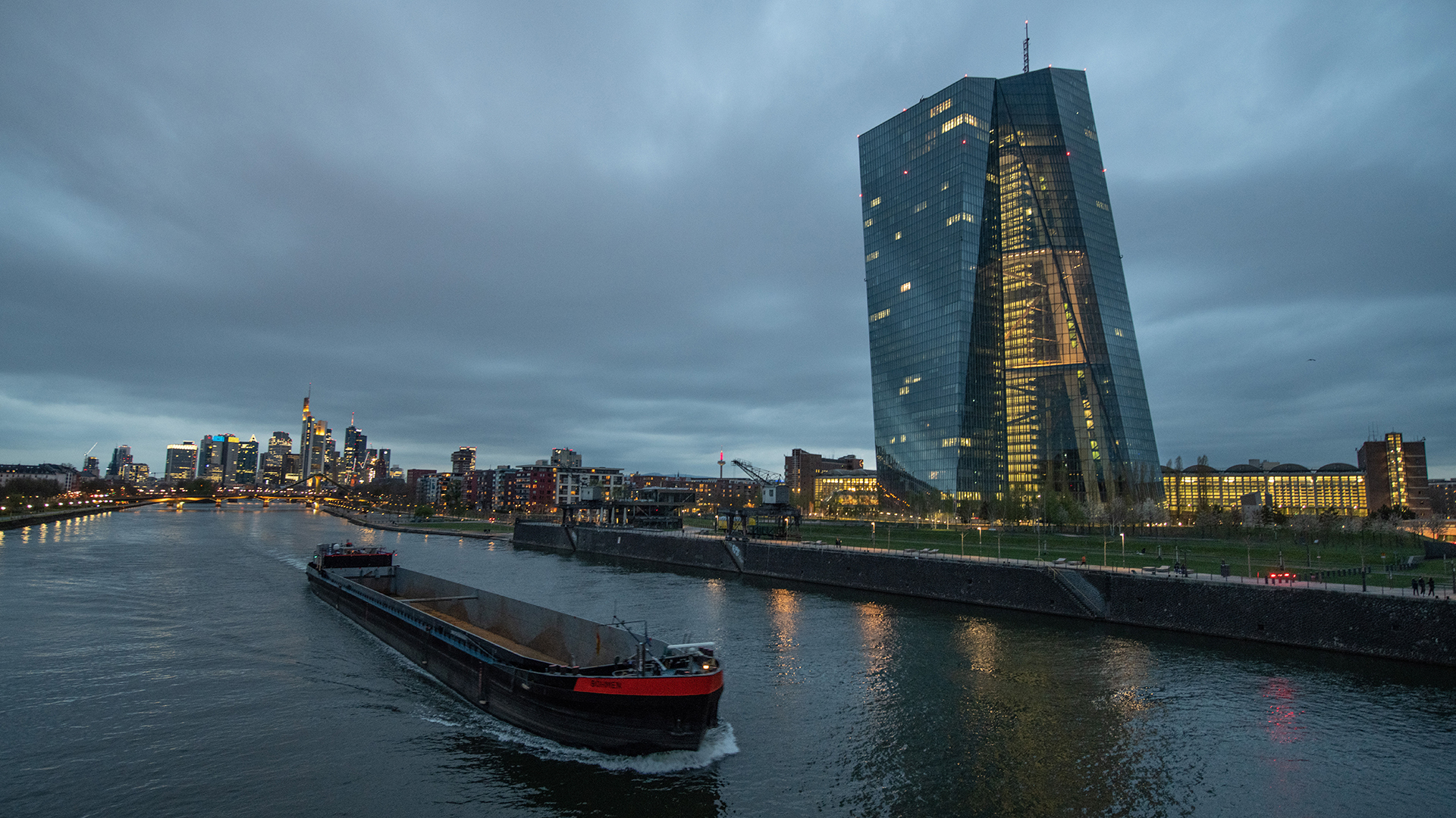 Ein Binnenschiff fährt im letzten Licht des Tages vor der Bankenskyline der Innenstadt über den Main an der EZB (Europäische Zentralbank) vorbei. | dpa