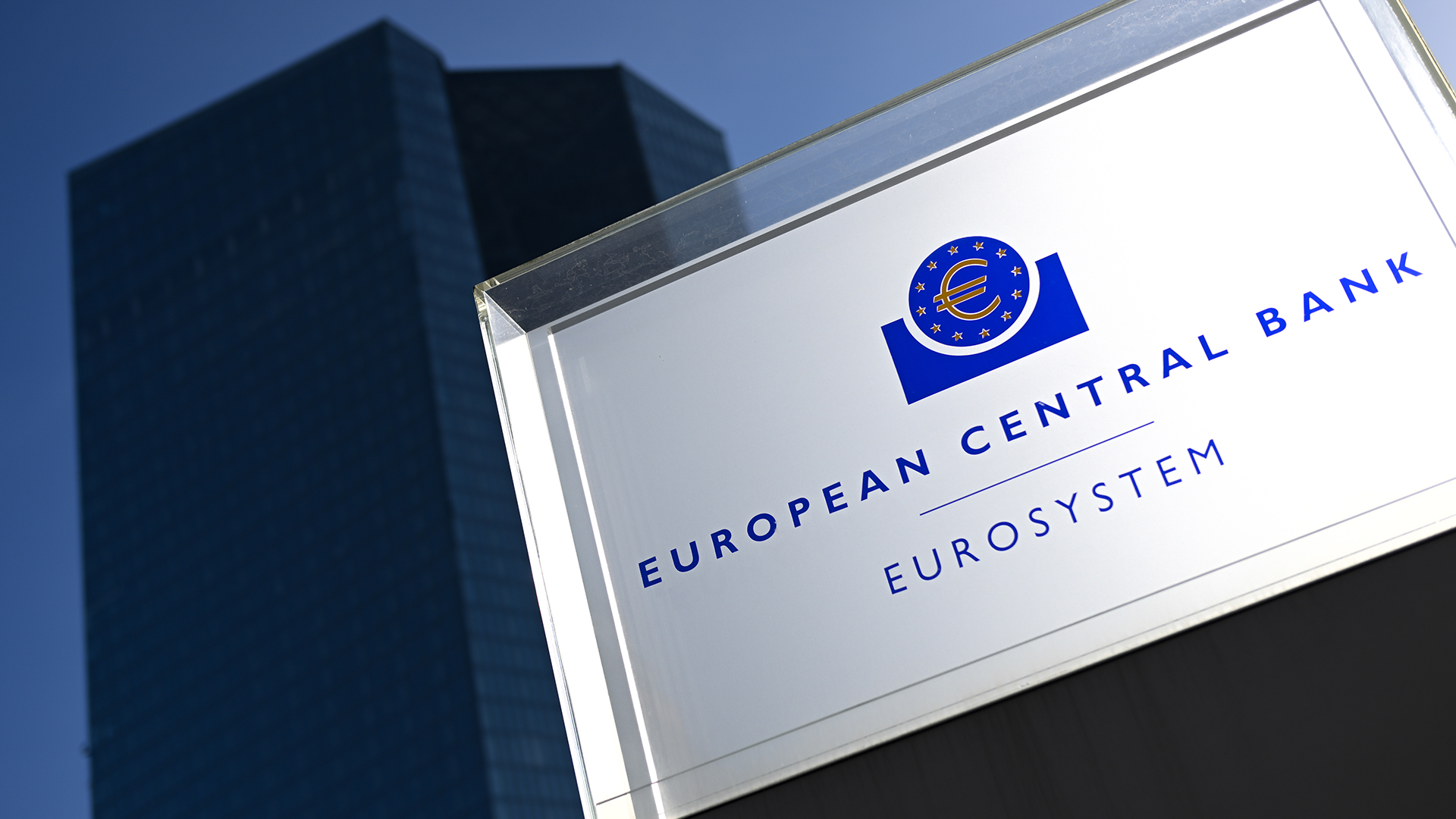 Die Sonne beleuchtet vor der Zentrale der Europäischen Zentralbank (EZB) eine Stele mit einem Schild, das die Aufschrift "European Central Bank Eurosystem" trägt. | dpa