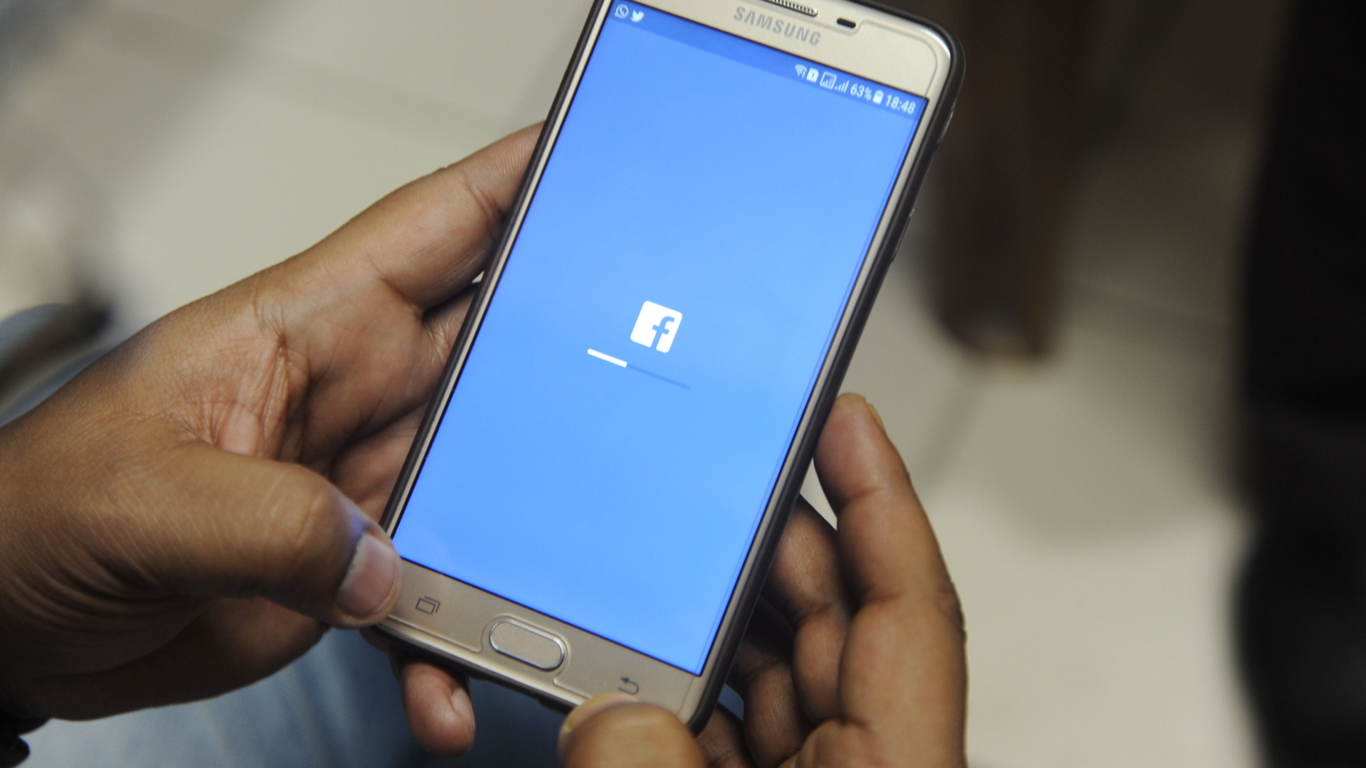 Eine Hand hält ein Smartphone, auf dem sich die Facebook-App aufbaut.