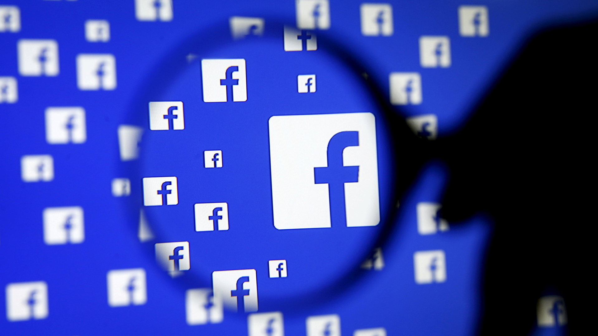 Ein Mann hält eine Lupe vor das Facebook-Logo. | REUTERS