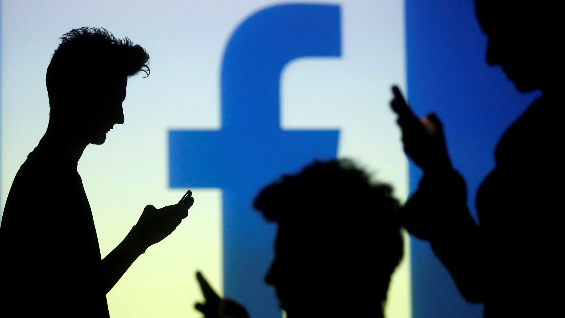 Silhouetten von Menschen mit Smartphone vor einem Facebook-Logo. | REUTERS