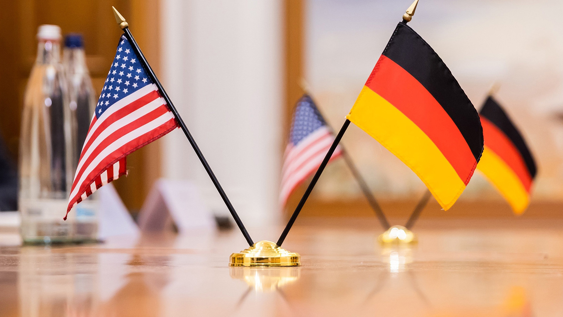 Fahnen von USA und Deutschland auf einem Konfernztisch.