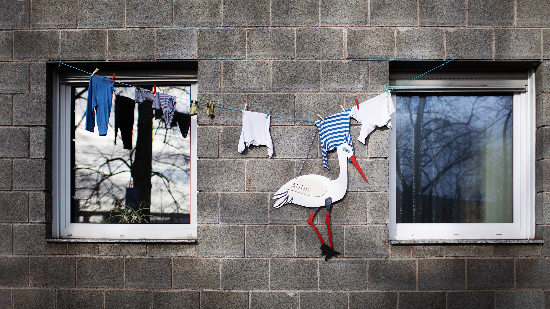 An einer Hauswand zeigt ein Klapperstorch und Kinderkleidung auf einer Leine die Geburt eines Kindes an. | picture alliance / photothek
