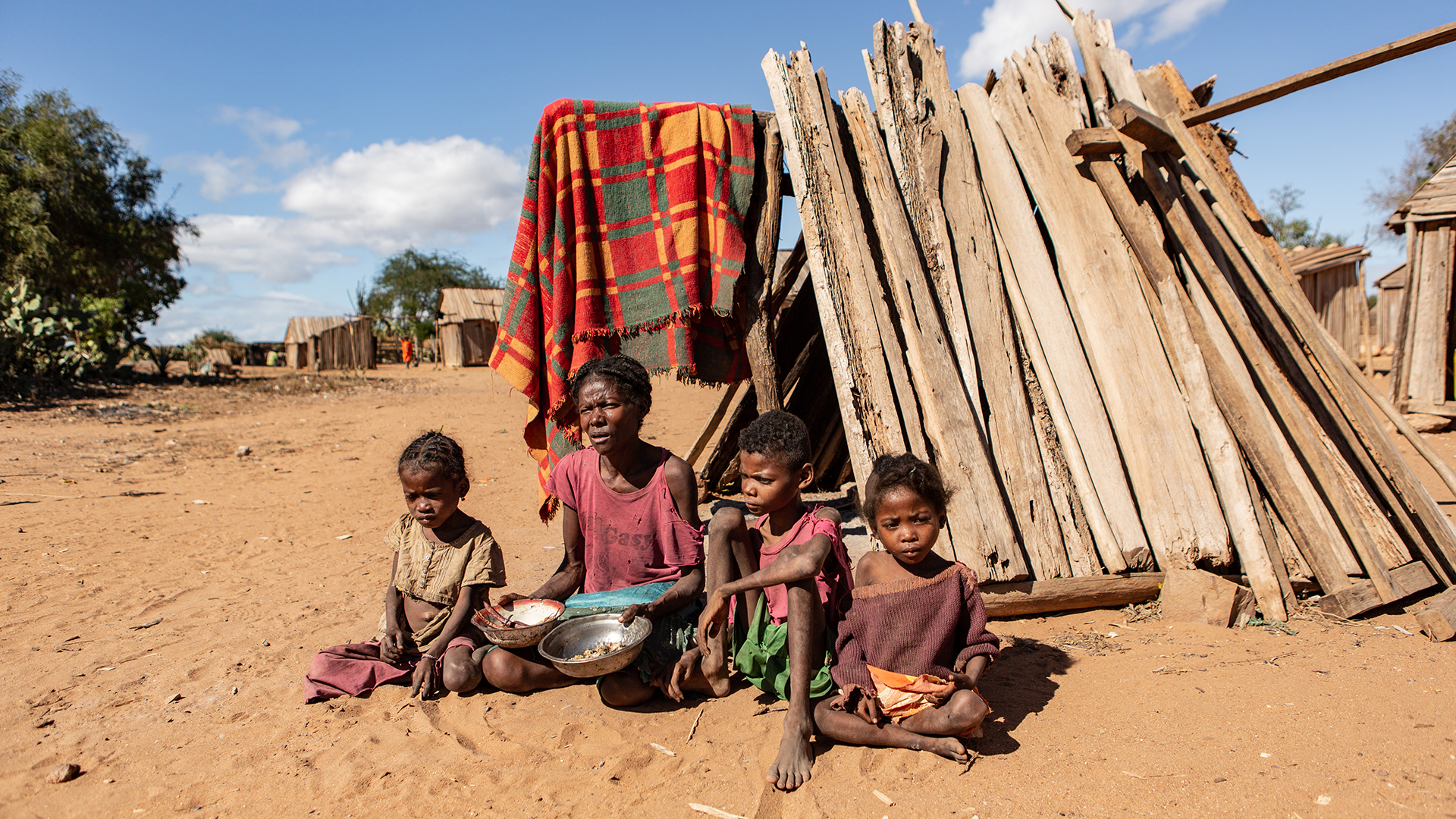 Eine Frau sitzt in Torovelo (Madagaskar) mit ihren Kindern vor einer Hütte aus Holzbalken. | dpa