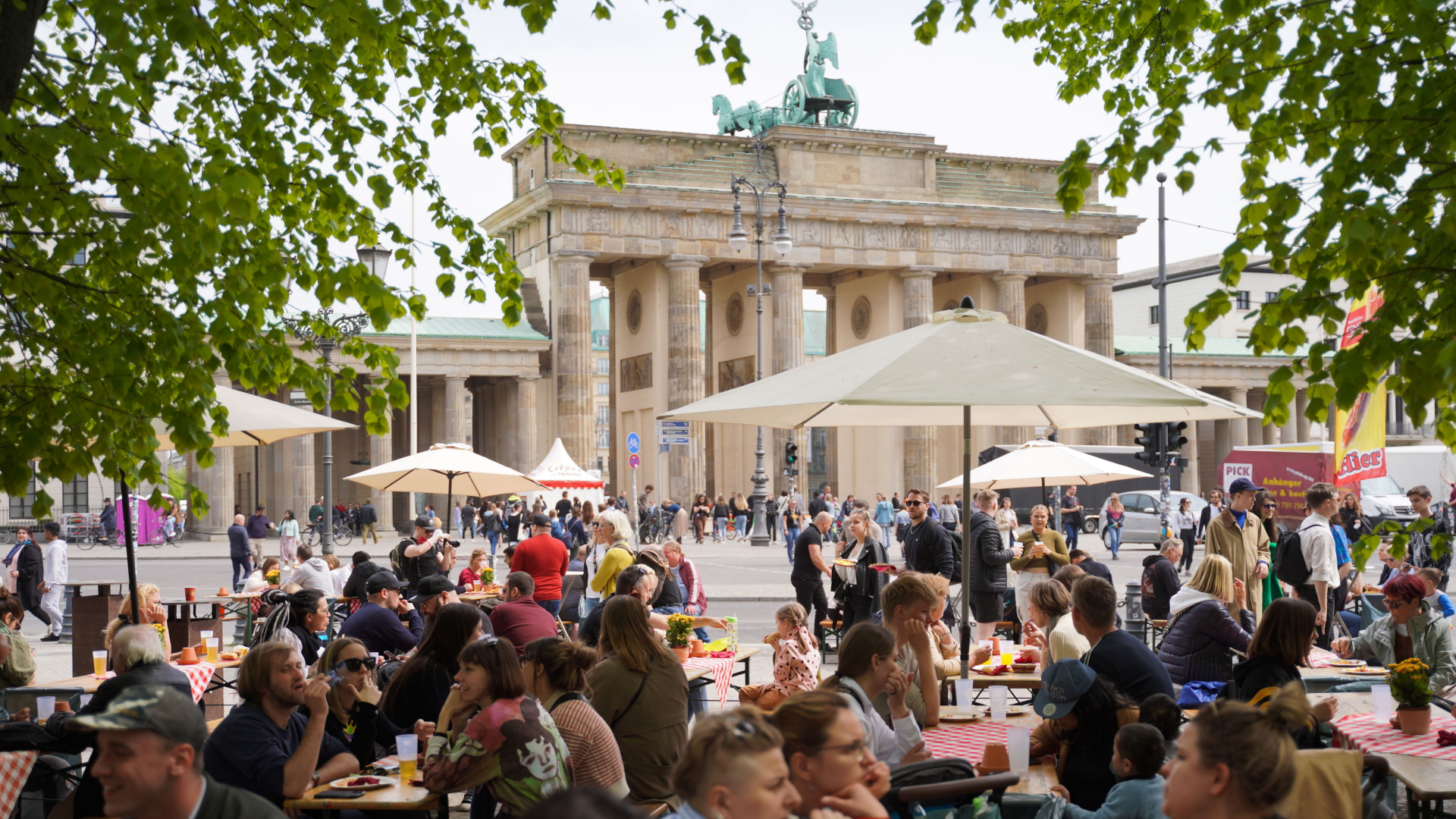 Menschen in Berlin sitzen vor dem Brandenburger Tor auf Bierbänken und genießen das schöne Wetter. | dpa
