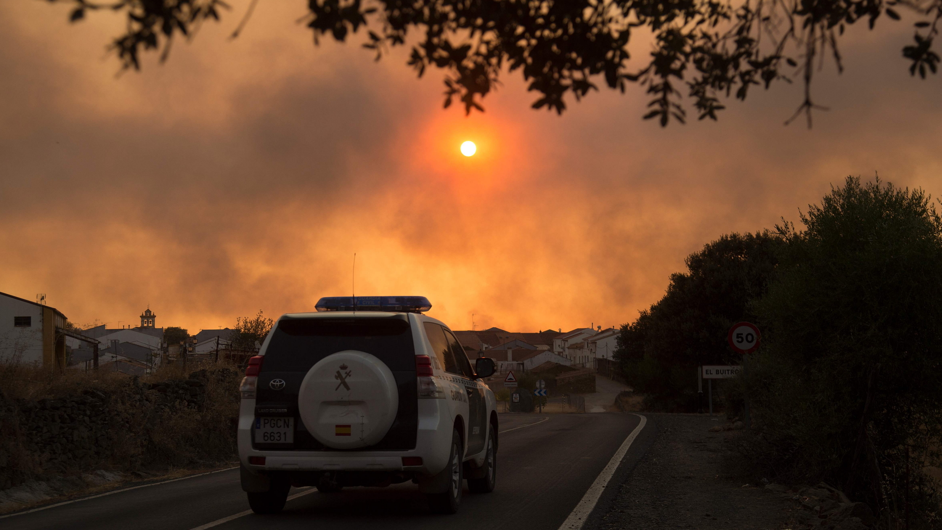 Ein Fahrzeug des Zivilschutzes fährt auf einer Straße in El Buitron, Huelva, Spanien, während im Vordergrund Rauch von Waldbränden aufsteigt. | AFP