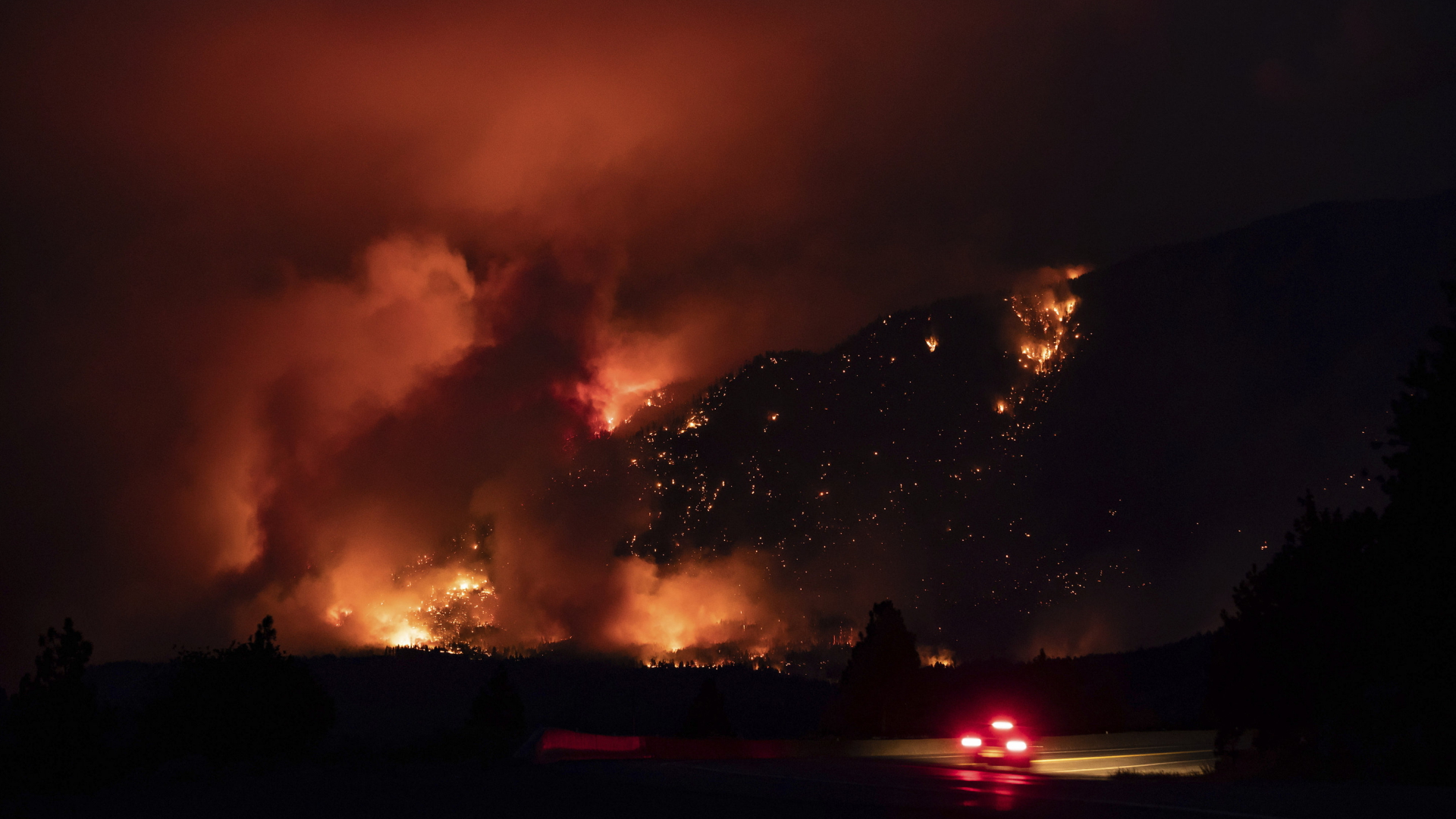 Ein Auto steht auf einer Straße vor einer mächtigen Feuersbrunst. | AP