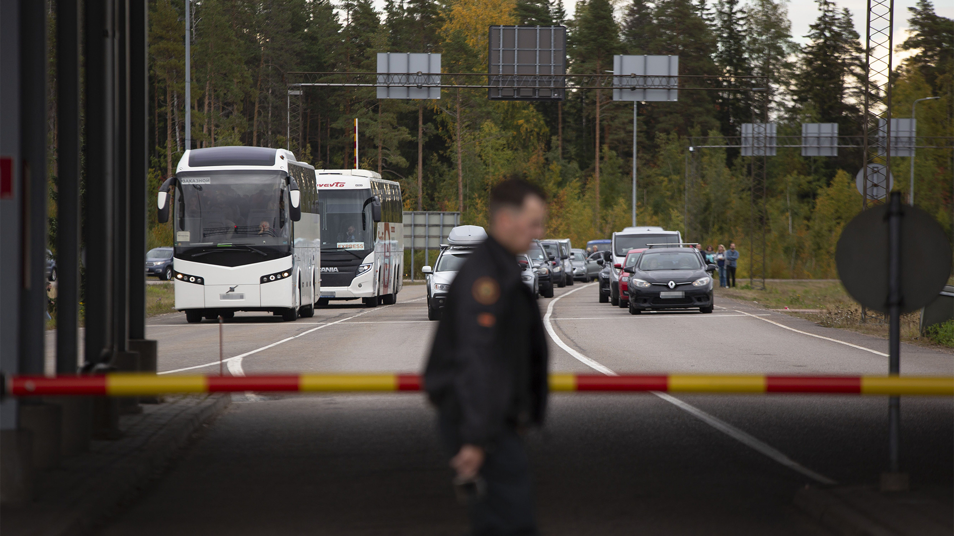 Ein Grenzschutzbeamter geht an einer Schranke vorbei, während Autos und Busse am Grenzübergang Vaalimaa darauf warten, die Grenze von Russland nach Finnland zu passieren. | dpa