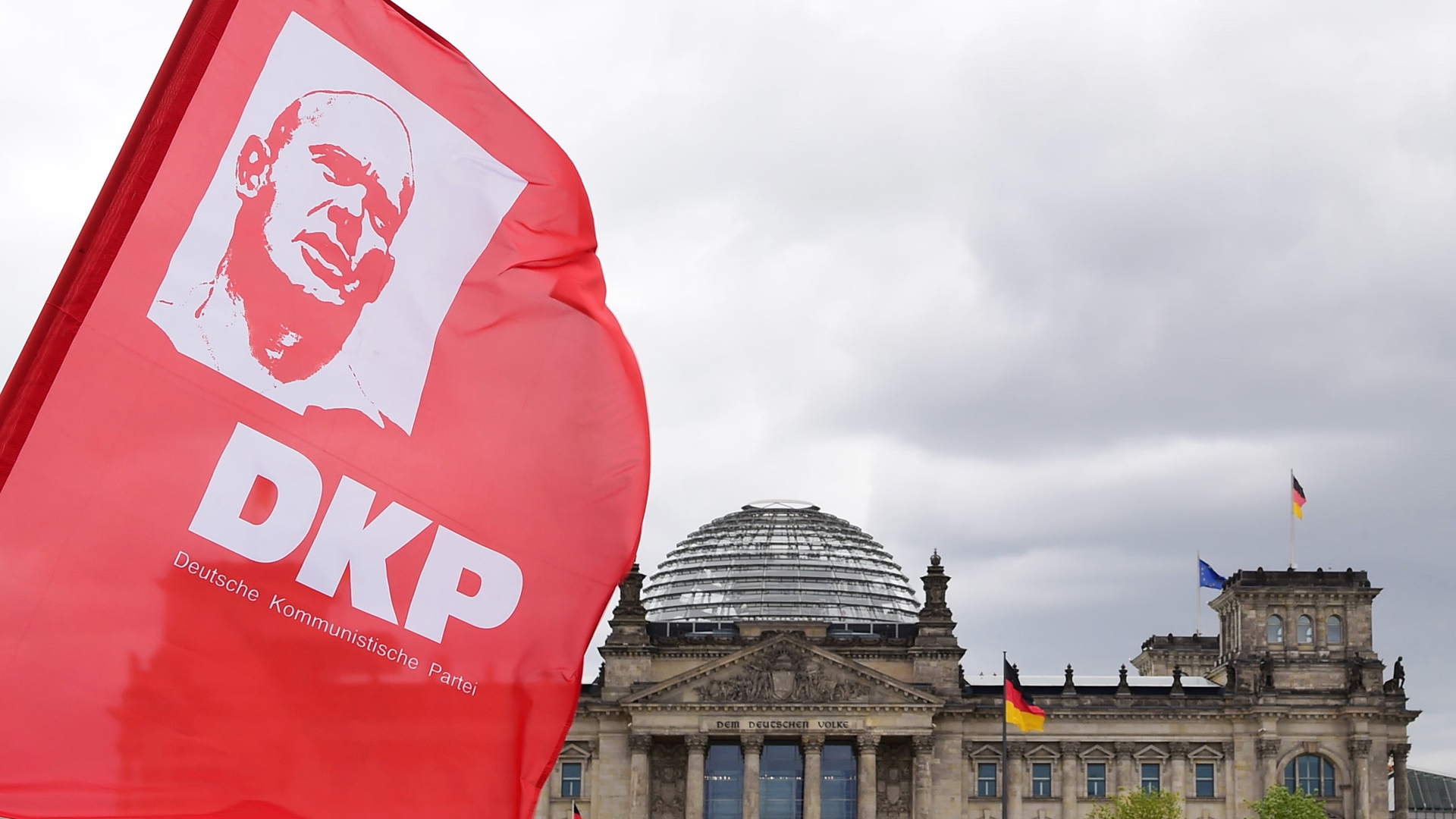 Eine rote Flagge der DKP mit dem Porträt von Ernst Thälmann weht vor dem Reichstagsgebäude in Berlin.  | picture alliance / dpa