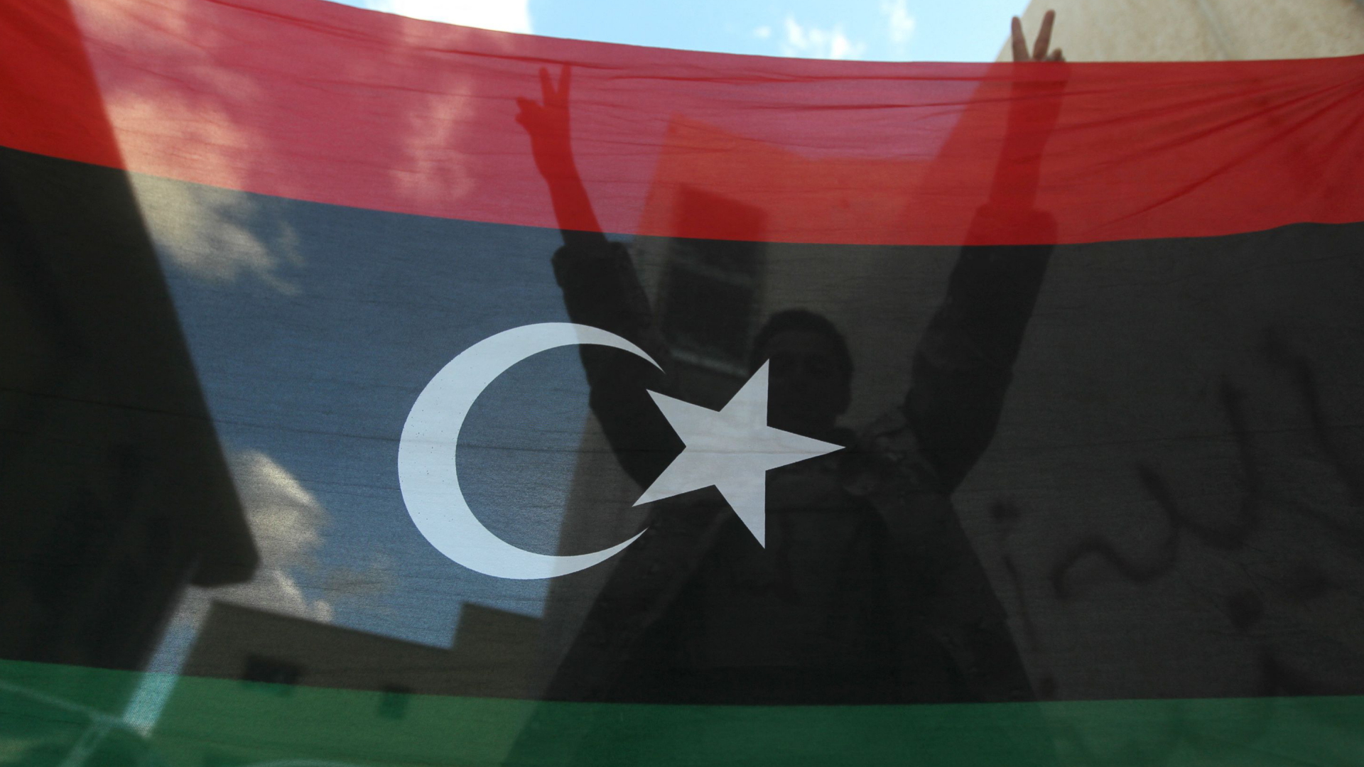 Ein Mann macht das Siegeszeichen hinter einer libyschen Flagge.  | AFP