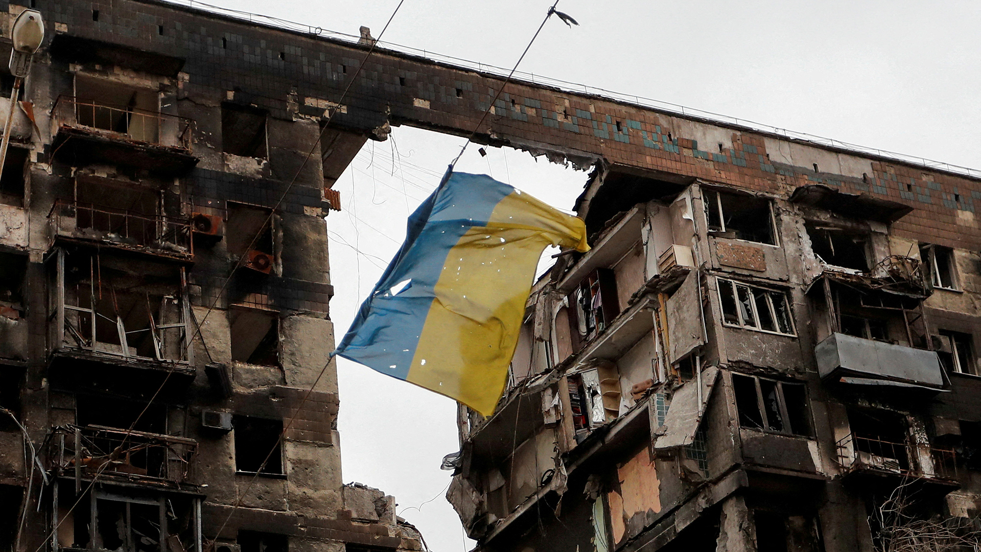 Eine zerrissene ukrainische Flagge hängt an einem Draht vor einem Wohnhaus, das während des ukrainisch-russischen Konflikts in der südlichen Hafenstadt Mariupol (Ukraine) am 14. April 2022 zerstört wurde. | REUTERS