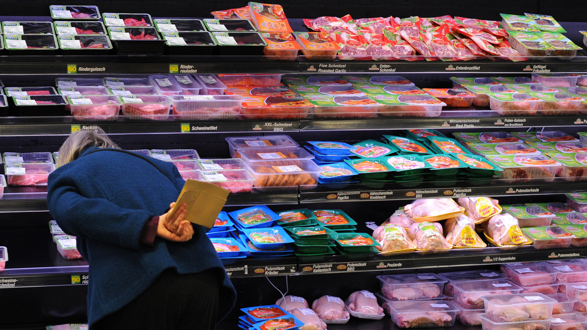 Eine Frau steht vor einem Supermarktregal mit abgepacktem Fleisch
