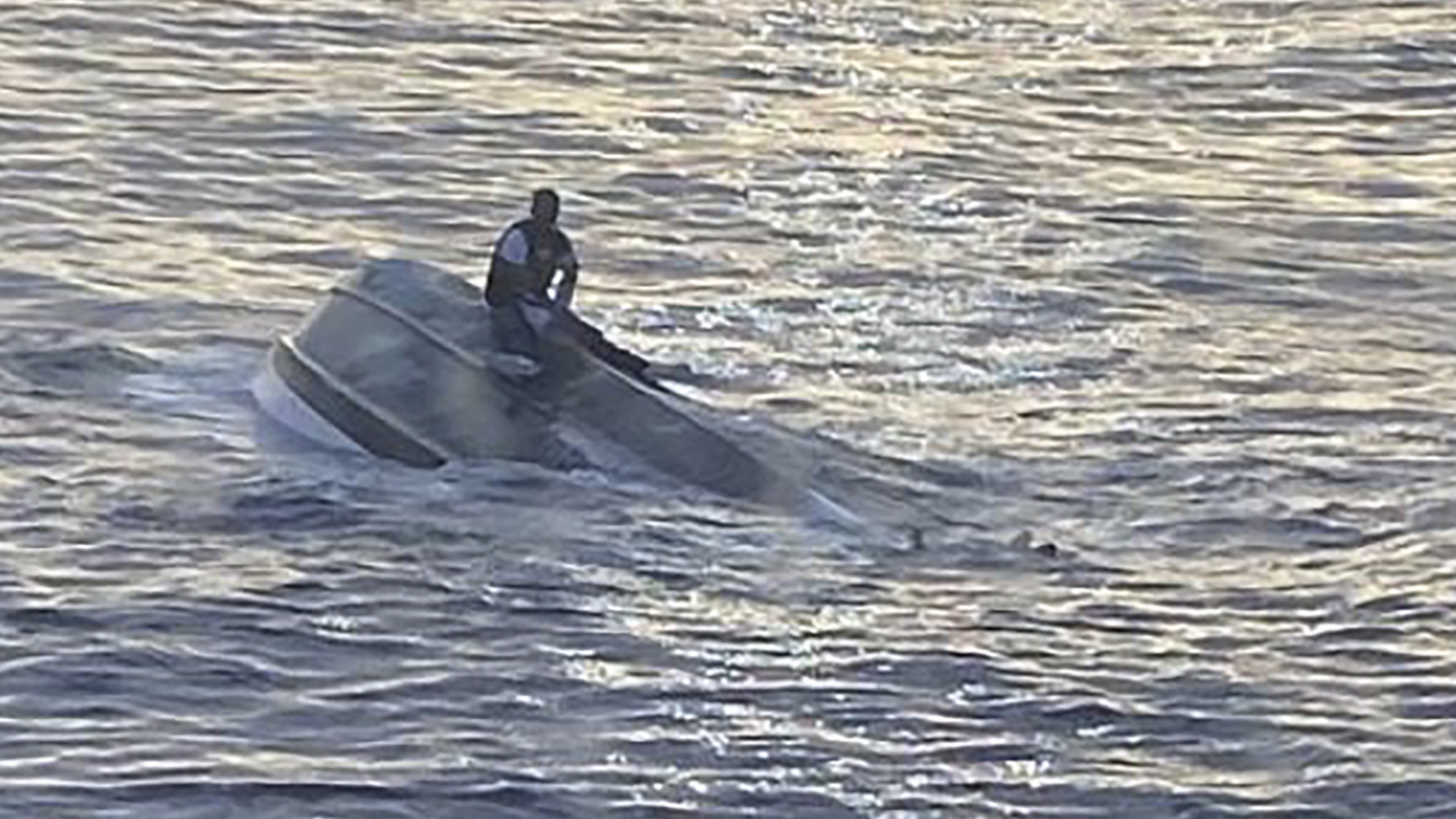Ein Mann sitzt auf dem Rumpf eines Bootes, das etwa 70 Kilometer vor der Küste Floridas gekentert ist. | AFP