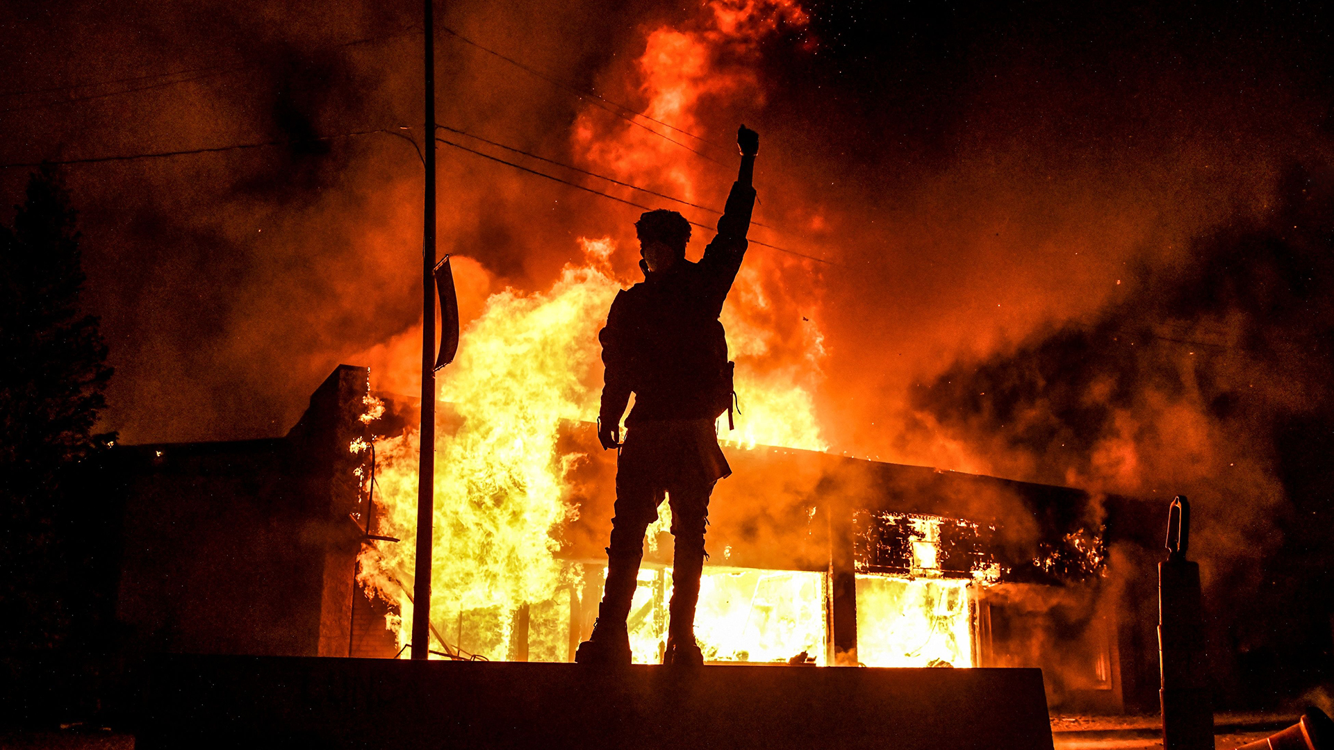 Ein Demonstrant mit erhobener Faust steht vor einem brennenden Gebäude, das während einer Demonstration in Minneapolis, Minnesota, in Brand gesteckt wurde. | AFP