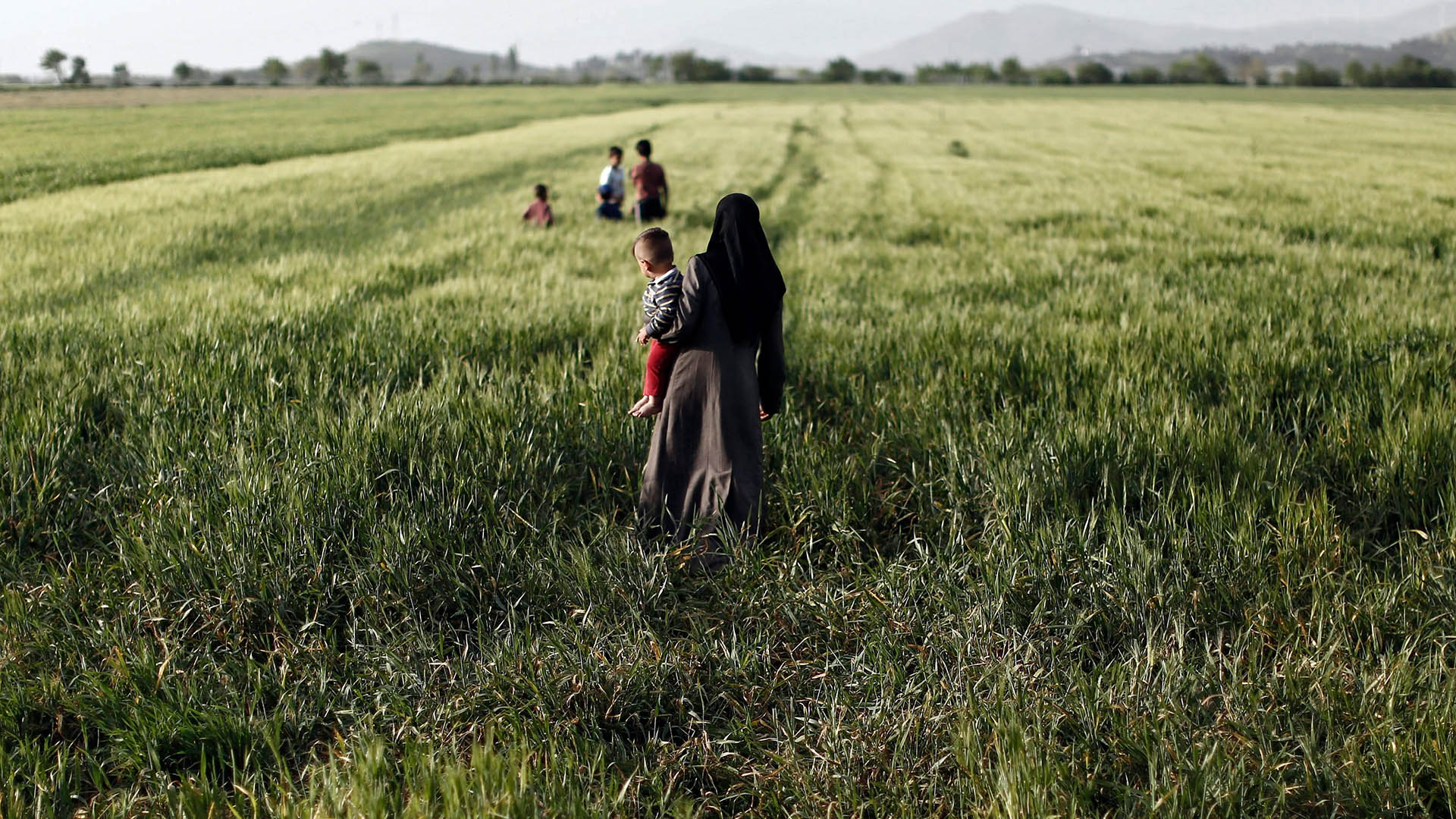 Eine syrische Flüchtlingsfrau geht mit ihrem Kind im Arm durch ein Feld im Flüchtlingslager nahe der griechisch-mazedonischen Grenze bei Idomeni. (Archivbild: 14.04.2016) | picture alliance / dpa