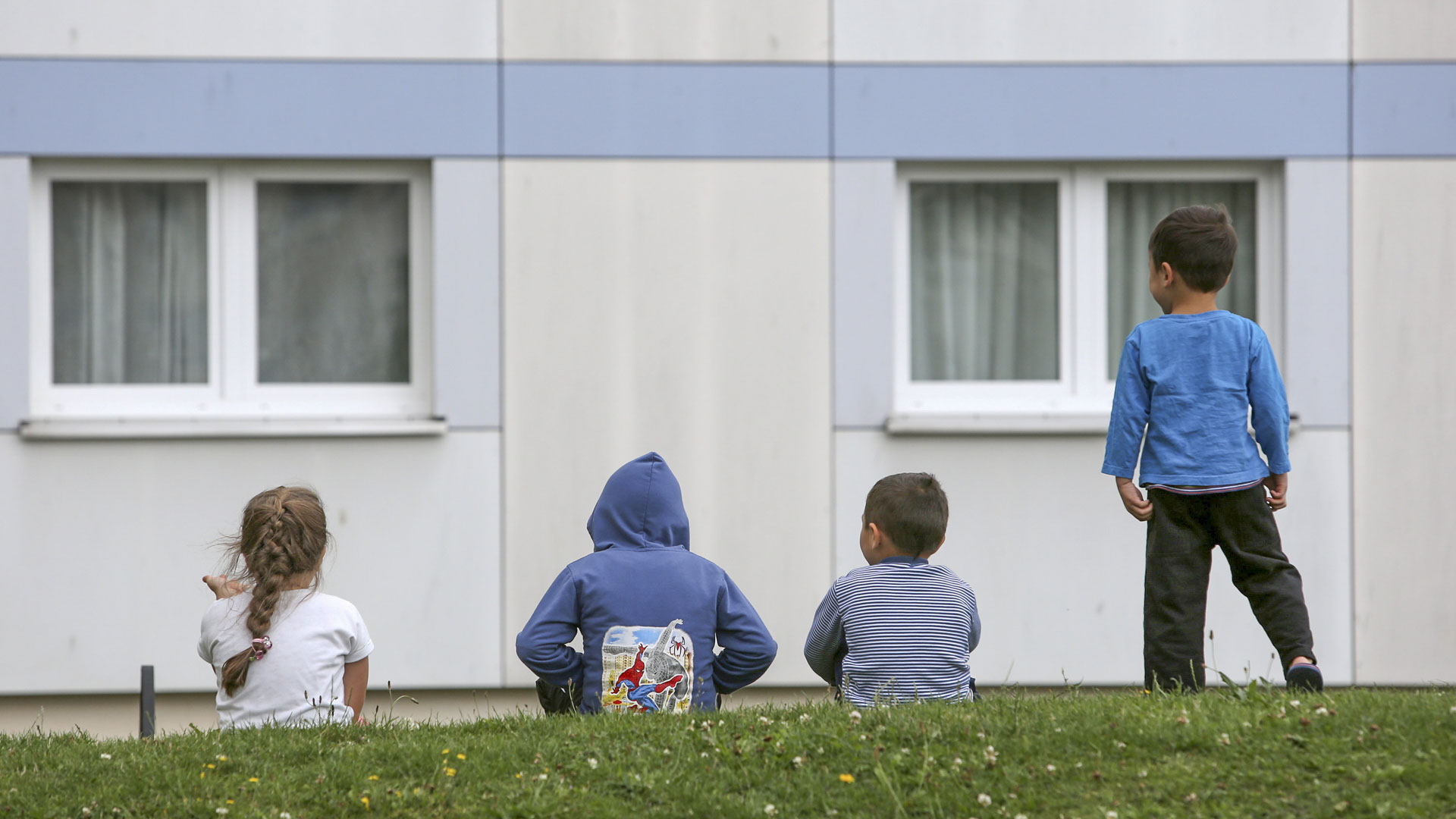 Kinder sitzen auf einer Wiese vor einem Flüchtlingsheim.