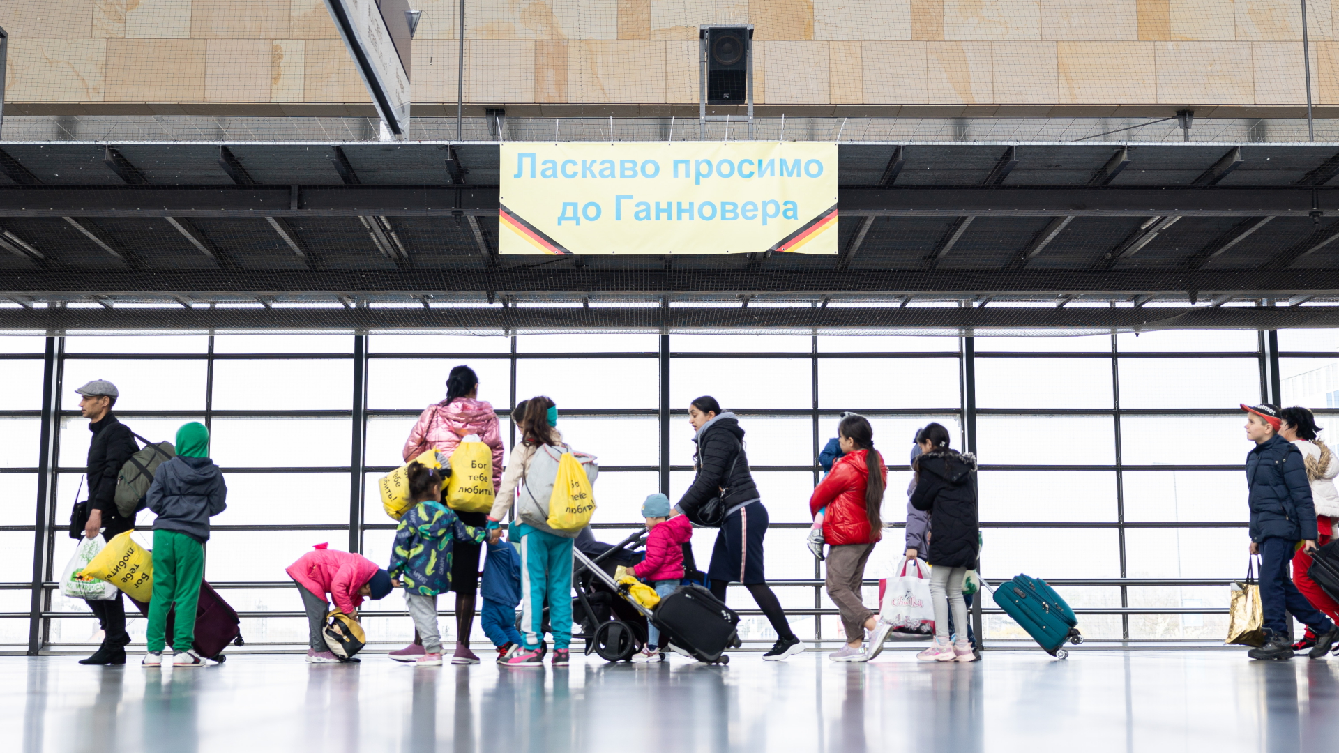 Geflüchtete aus der Ukraine gehen durch die Eingangshalle vom Messebahnhof Laatzen. Auf einem Banner im Hintergrund steht "Willkommen in Hannover" auf Ukrainisch.