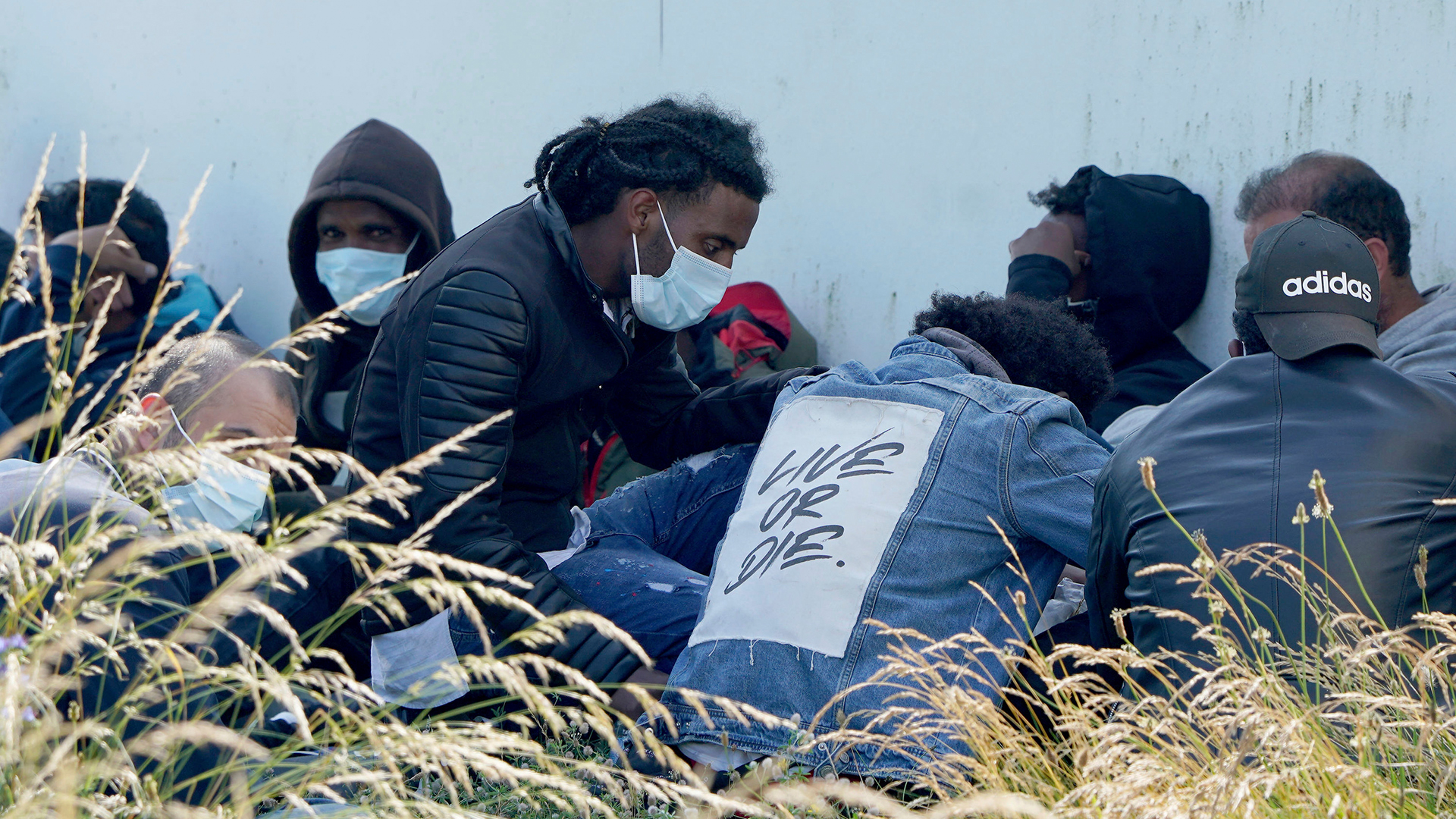  Eine Gruppe von Menschen sitzt an einer Wand, nachdem sie von Beamten der Border Force in Dungeness, Südengland, vom Strand eskortiert wurden. | AP