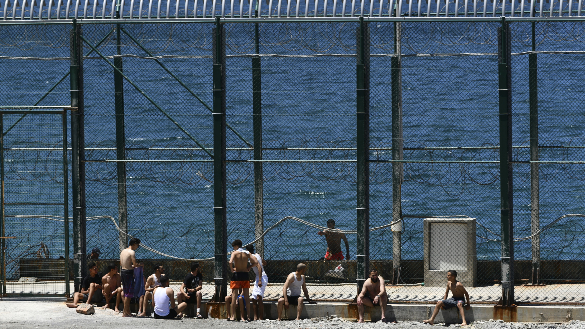 Männer und Kinder aus Marokko sitzen an einem Zaun am Meer nachdem sie spanisches Festland in Ceuta erreicht hatten.  | AP