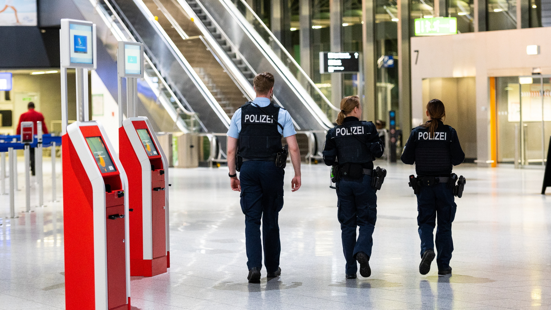Drei Polizisten gehen durch das Terminal 1 am Flughafen. 