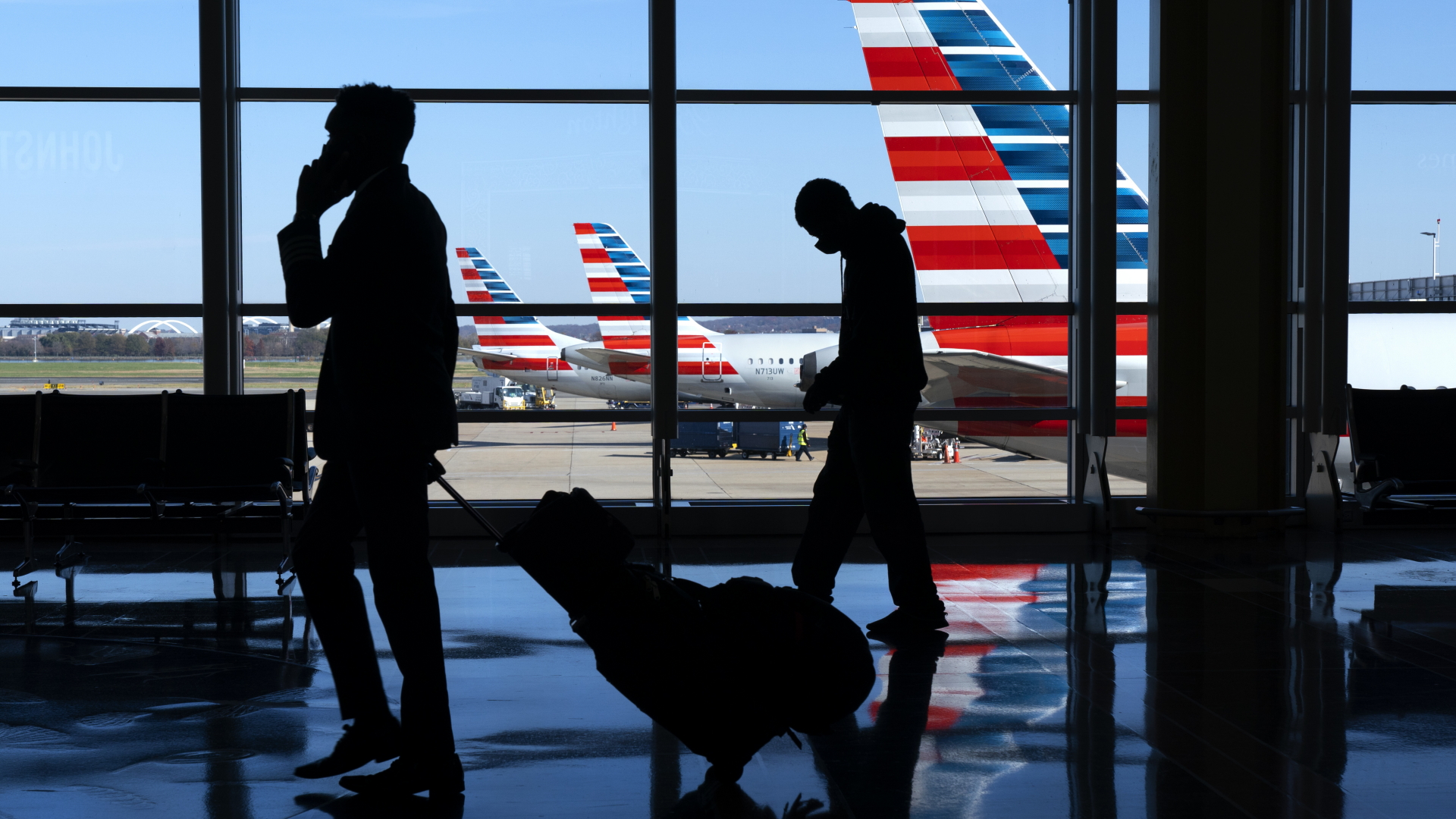 Flugreisende gehen am Flughafen "Ronald Reagan Washington National Airport" vor einer Glasfront, durch die man Flugzeuge der Fluggesellschaft "American Airlines" sehen kann. (Archivbild) | dpa