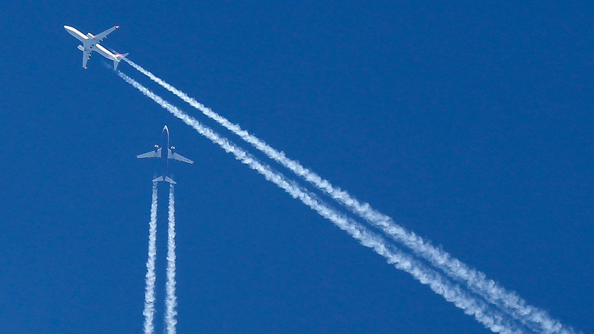 Die Wege zweier Flugzeuge kreuzen sich am Himmel. | picture alliance / Ina Fassbende