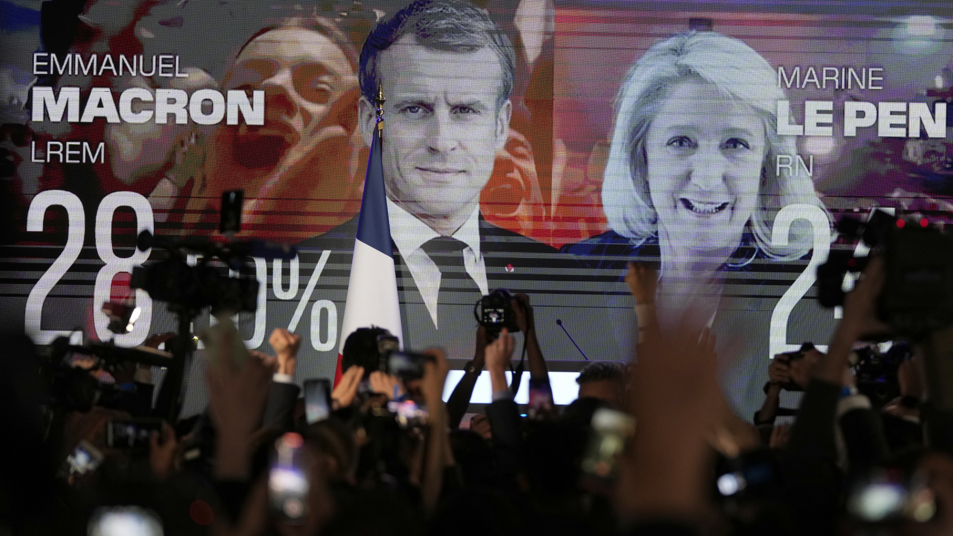Menschen stehen in Paris vor einem Bildschirm, der Frankreichs Präsident Emmanuel Macron und Marine Le Pen zeigt.