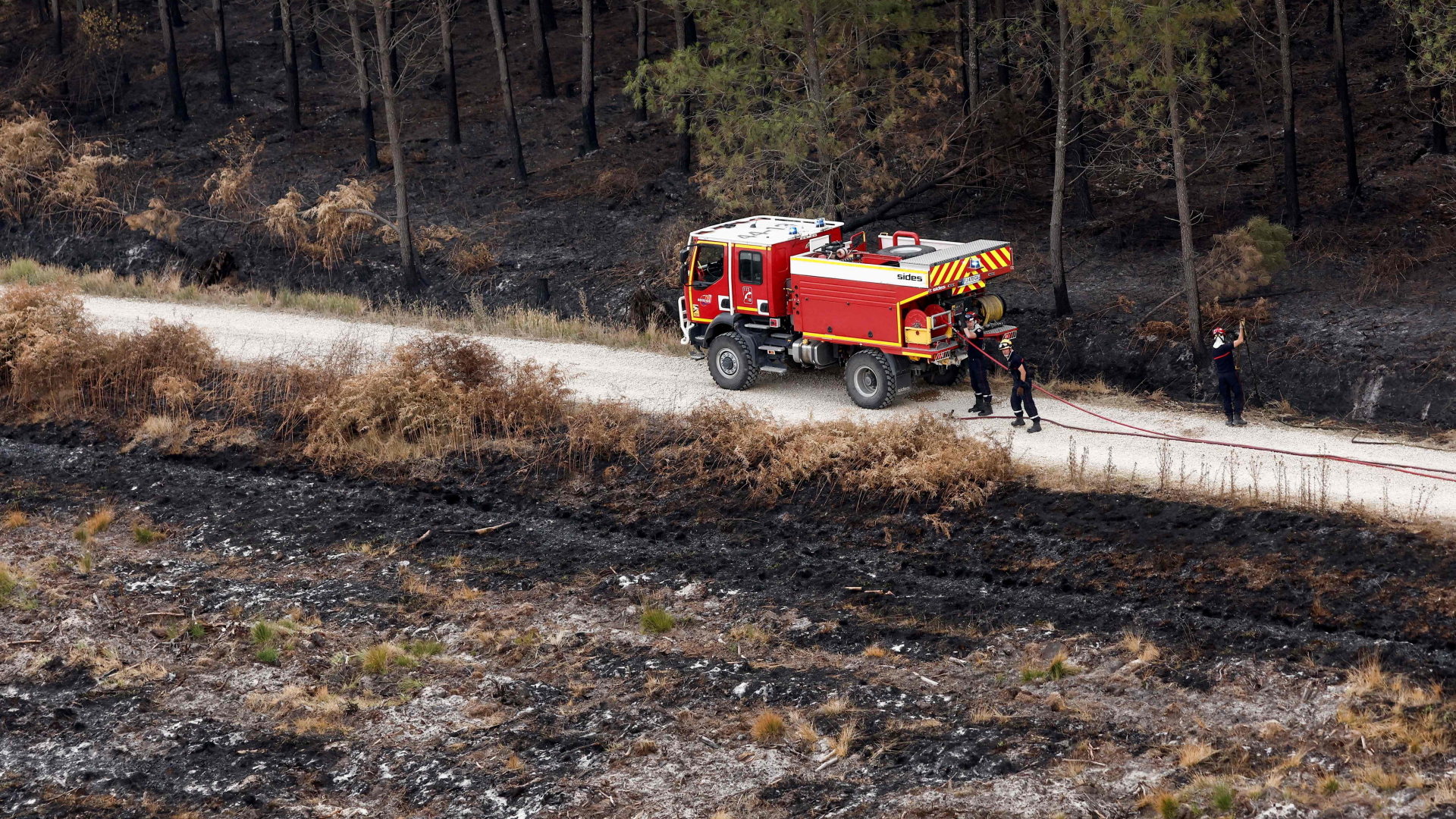 Feuerwehrleute mit ihrem Löschfahrzeug vor verbrannter Vegetation nahe Landiras in der Gironde-Region in Frankreich | AFP