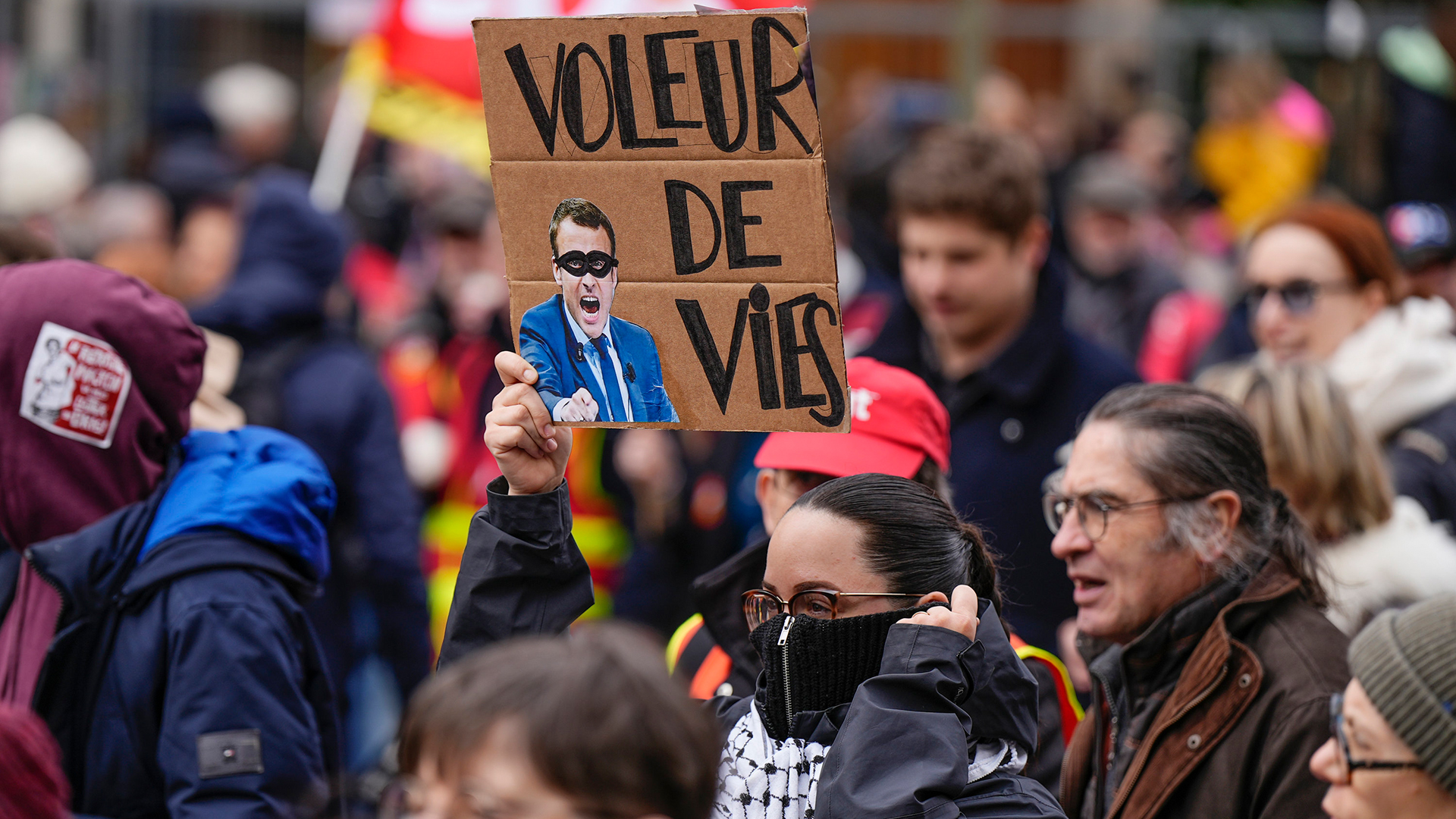 Ein Demonstrant hält während einer Demonstration in Paris ein Plakat mit einem Porträt des französischen Präsidenten Macron in der Hand. | AP
