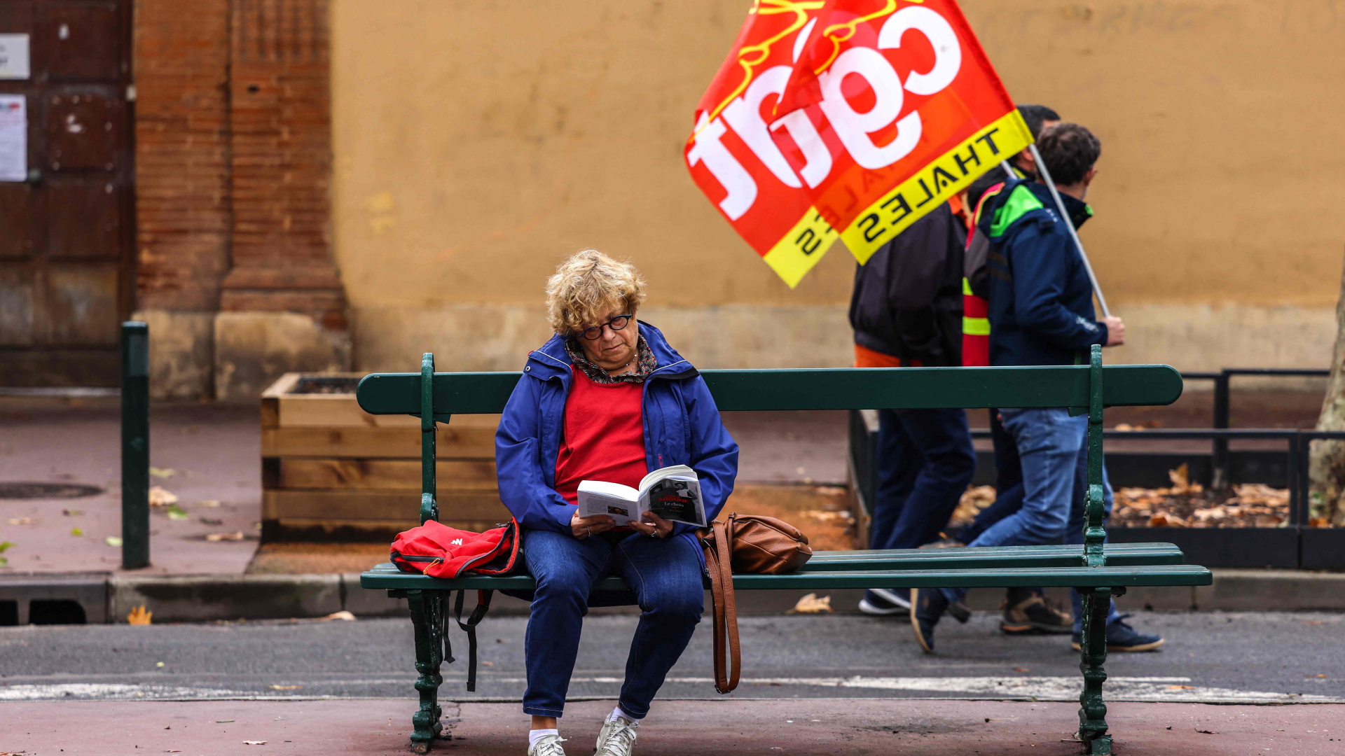 Eine Frau liest ein Buch, hinter ihr Demonstranten mit Fahnen der Gewerkschaft CGT, in Toulouse | AFP