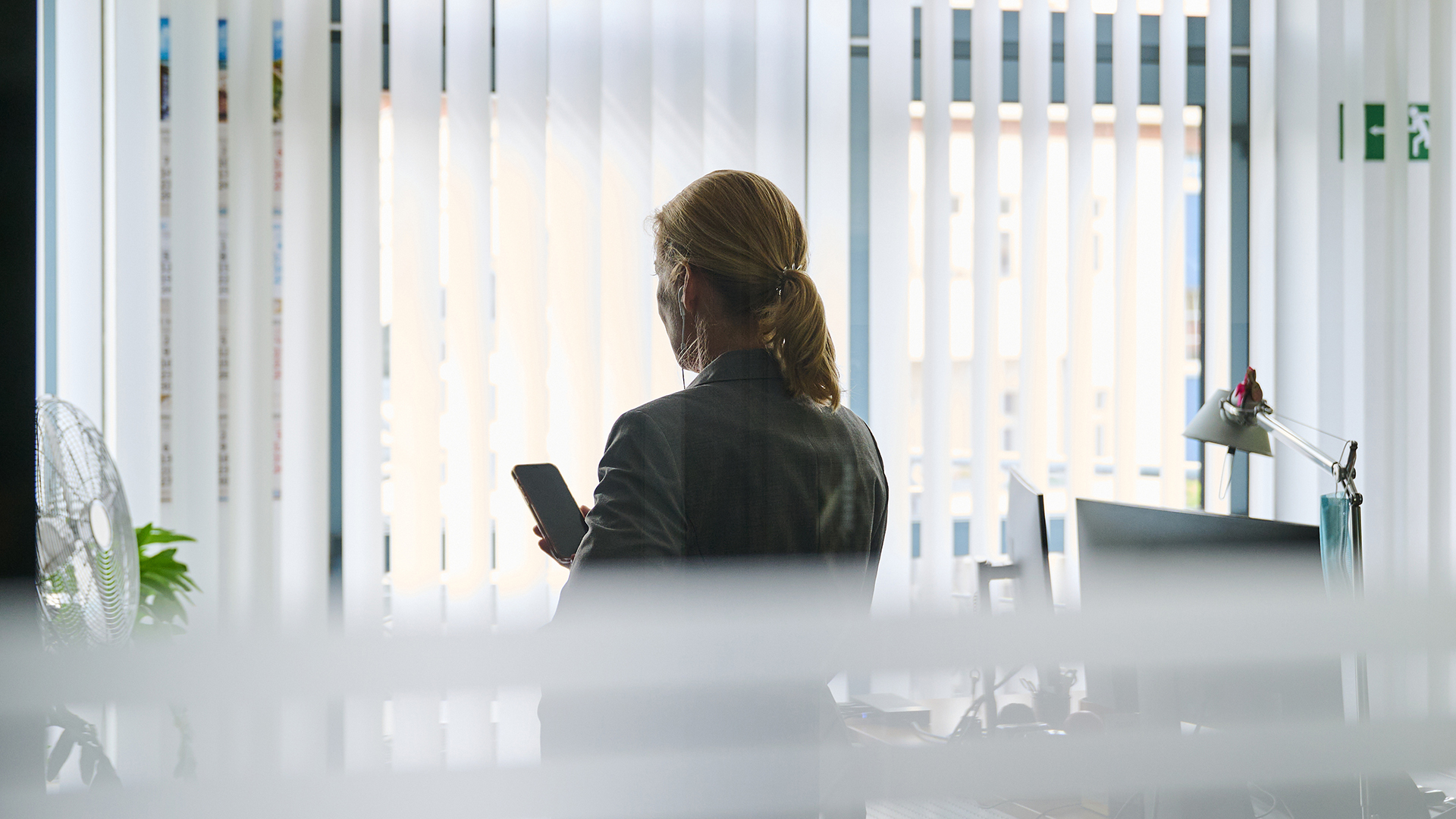 Eine Frau steht in einem Bürozimmer am Fenster und telefoniert über ein Headset. | picture alliance/dpa