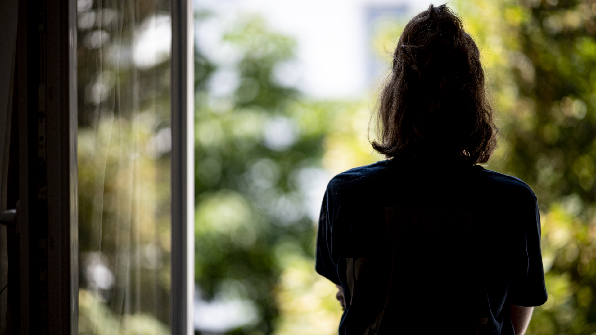 Eine Frau steht in ihrer Wohnung an einem Fenster. | Fabian Sommer/dpa