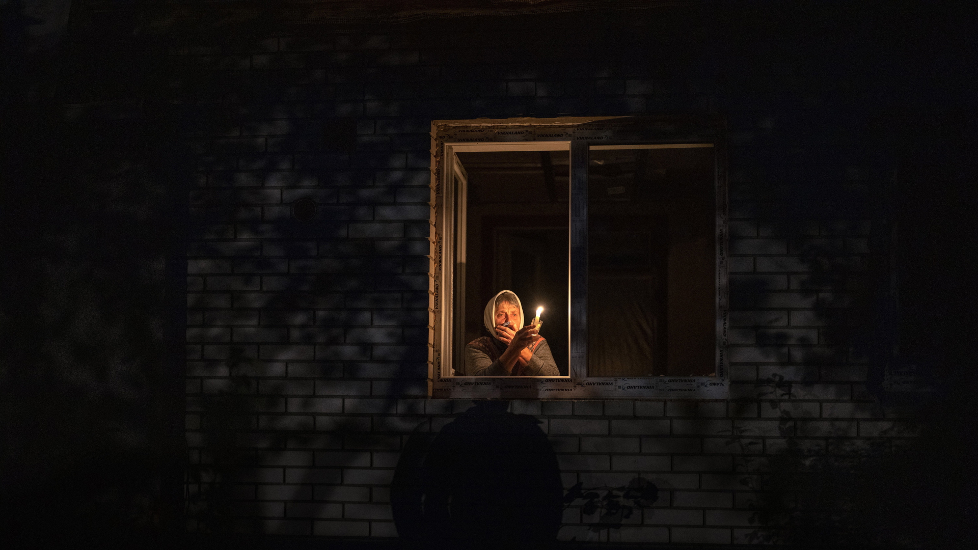 Eine Frau schaut während eines Stromausfalls in ihrem Haus in Borodyanka (Region Kiew) aus dem Fenster und hält eine Kerze. (Aufnahme vom 20. Oktober 2022) | AP