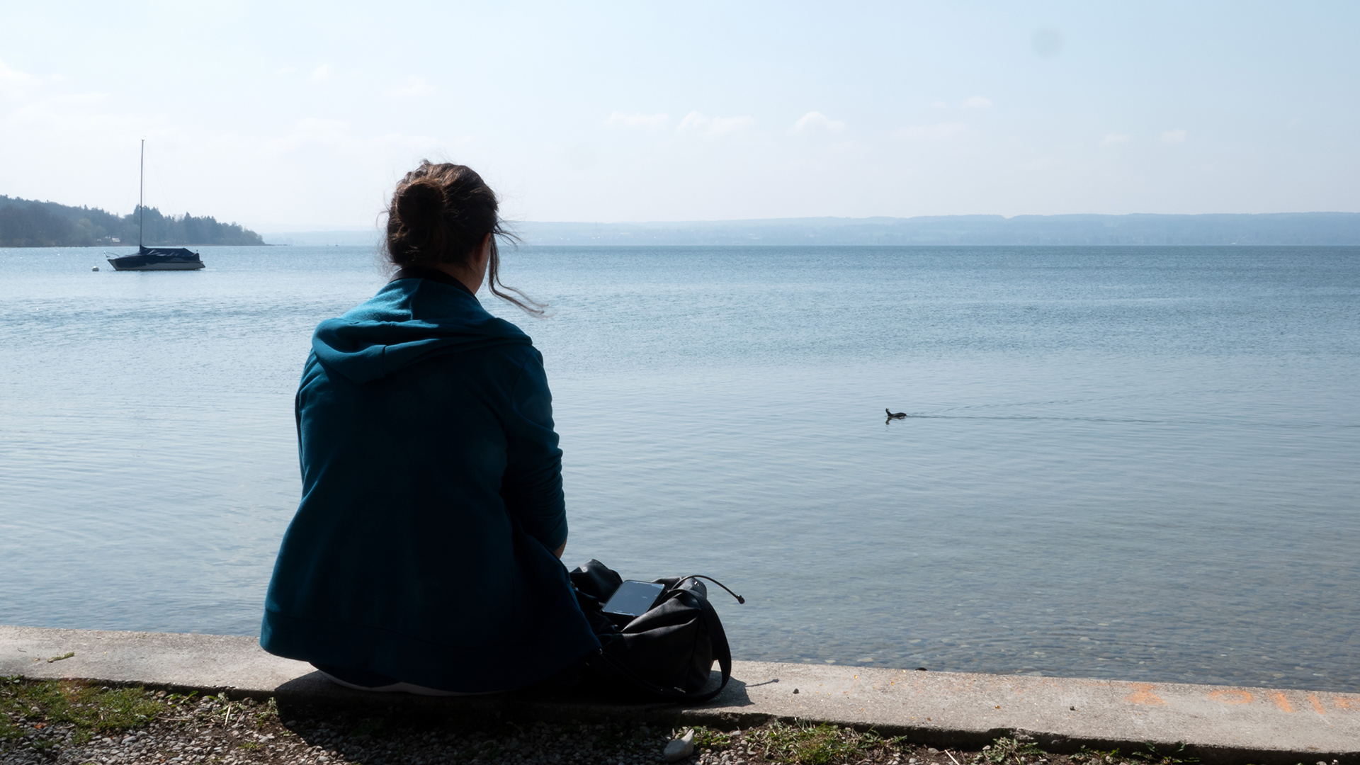 Eine Frau sitzt am Ammersee und blickt auf das Wasser.