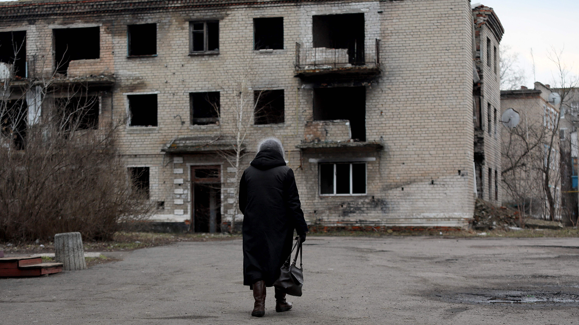 Eine Frau geht an einem alten, zerstörten Gebäude in der Kleinstadt Krasnogorivka in der Region Donezk vorbei. | AFP