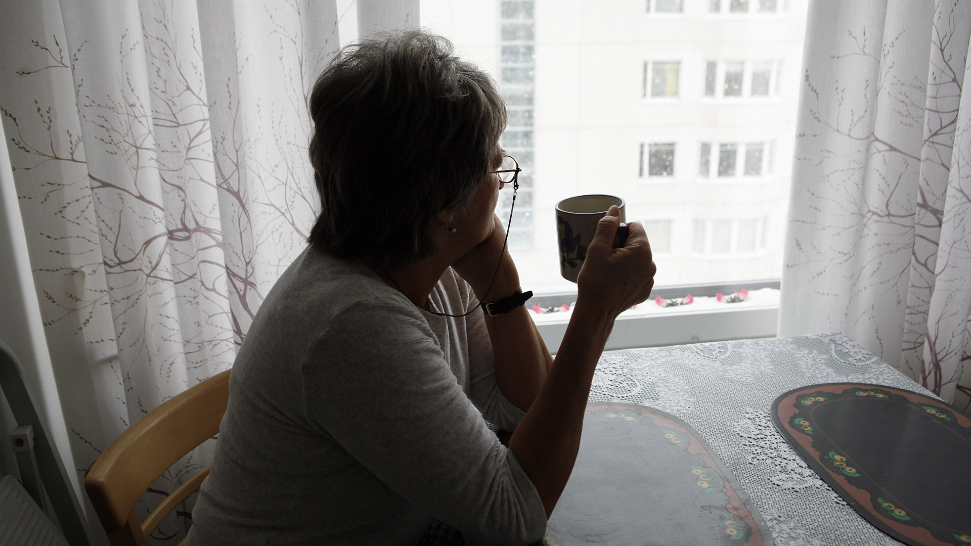Eine ältere Frau sitzt in ihrer Wohnung und guckt aus dem Fenster. | picture-alliance / Lehtikuva