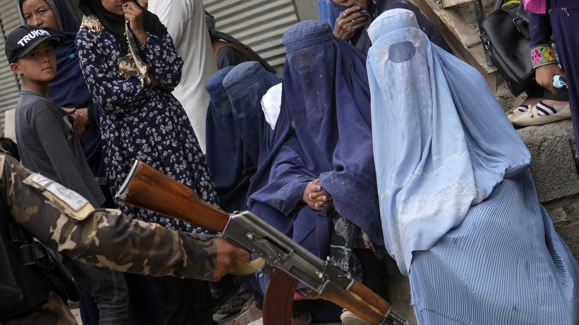 Ein Taliban-Kämpfer hält sein Gewehr in der Hand, während Menschen in Kabul auf die Verteilung von Lebensmitteln warten. | dpa