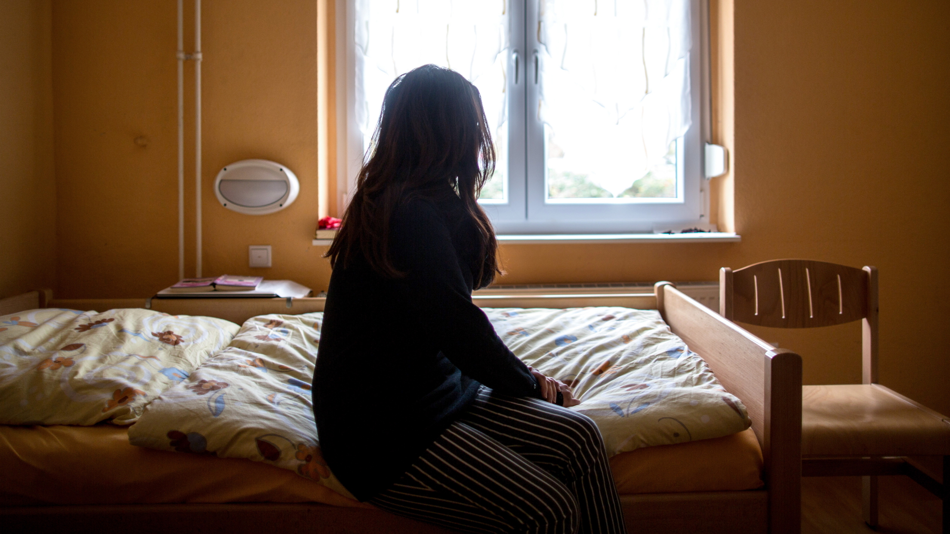 Eine Frau sitzt in einem Frauenhaus auf einem Bett.  | dpa