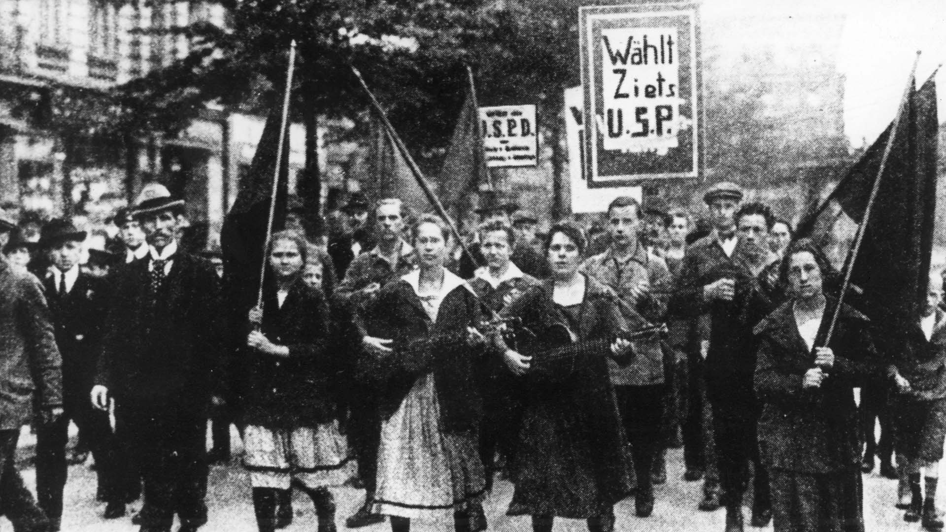 Unterstützerinnen der USPD demonstrieren mit Fahnen und Plakaten - in einer Aufnahme von 1919. | dpa