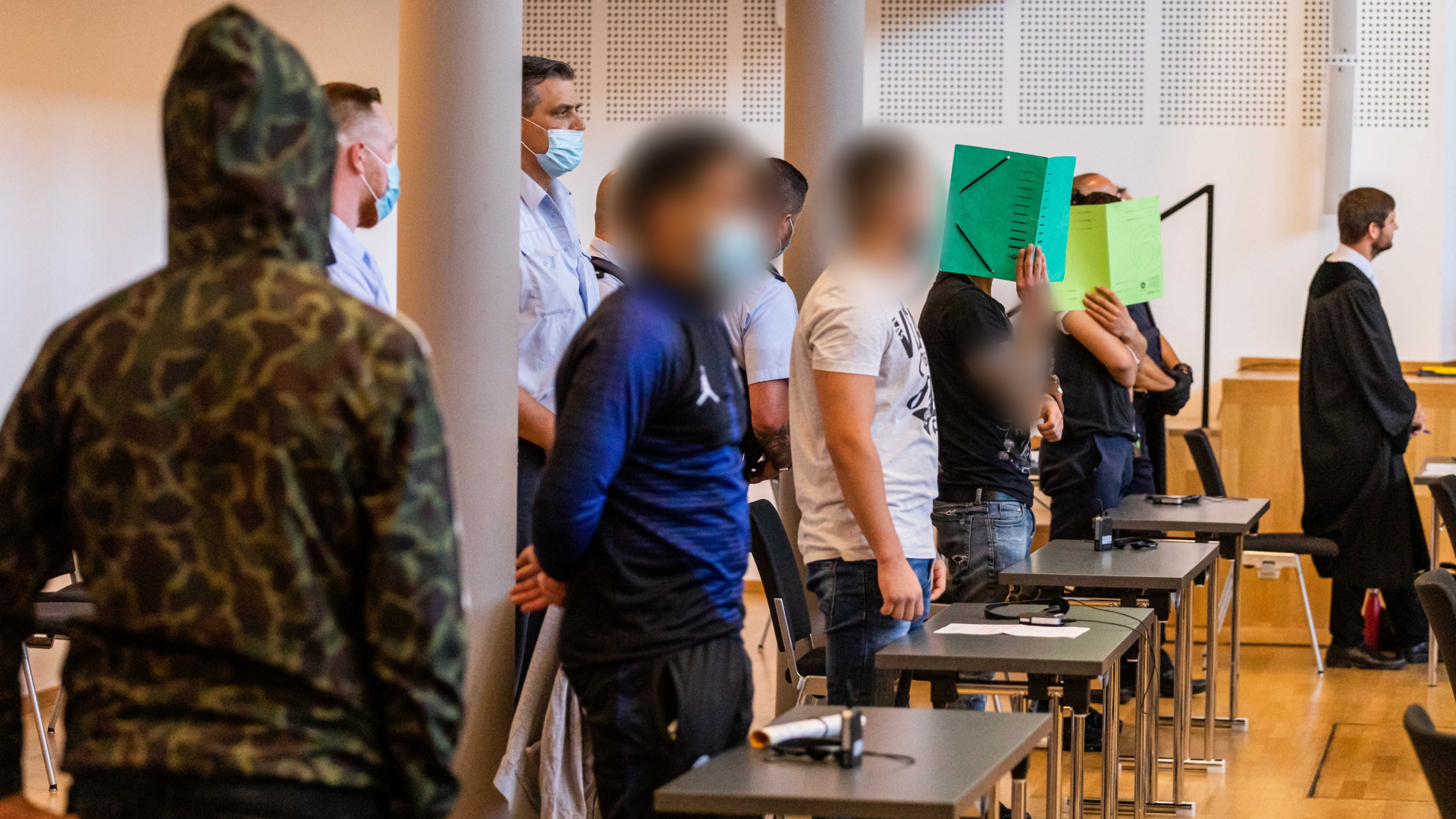 Fünf Angeklagte stehen hinter Tischen in einem Gerichtssaal in Freiburg. | dpa