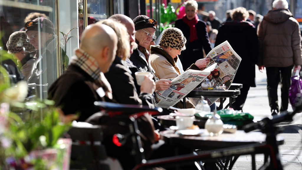 Menschen sitzen bei strahlendem Sonnenschein vor einem Cafe (Archivbild) | dpa