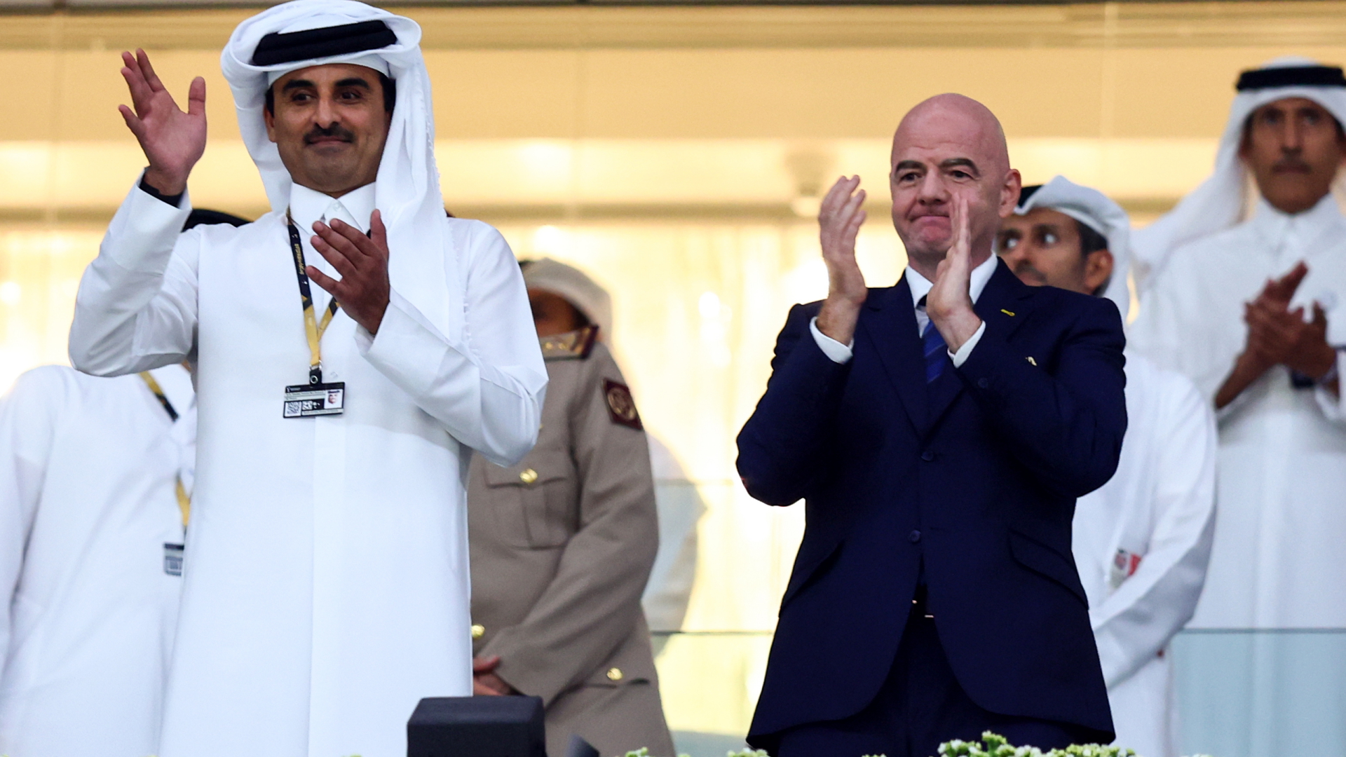 Der Emir von Katar, Scheich Tamim, winkt bei einem Spiel im Al-Bait Stadion in Katar ins Publikum - neben ihm steht FIFA-Präsident Gianni Infantino und applaudiert. | dpa