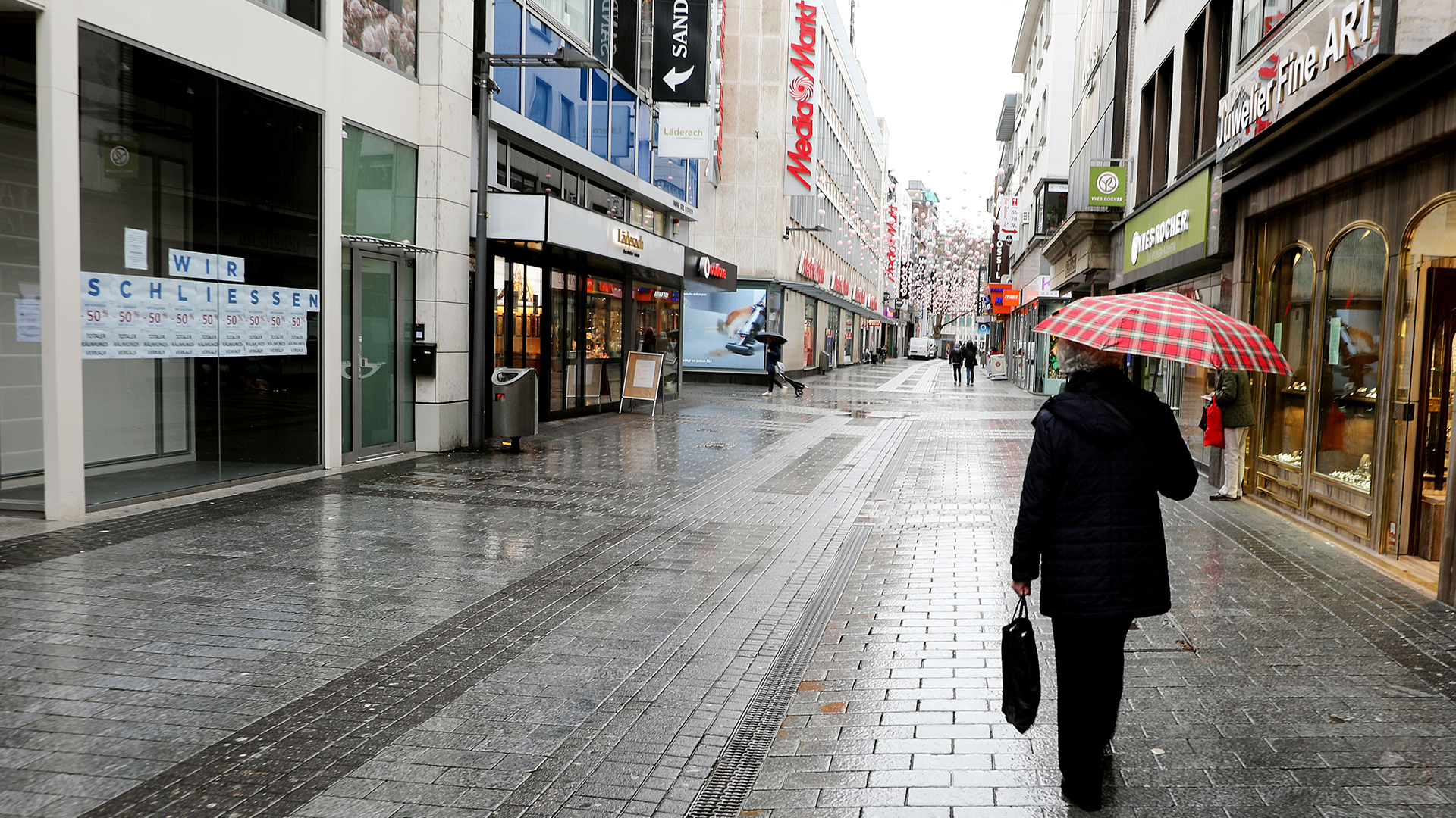 Eine Frau geht durch die leere Fußgängerzone Hohe Straße in Köln, an einem Schaufenster steht "Wir schließen"