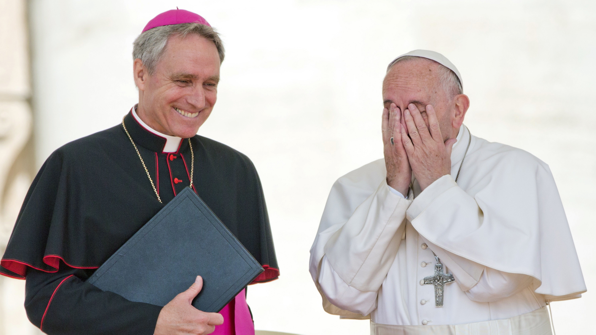 Georg Gänswein lächelt, während sich Papst Franziskus die Hände vor das Gesicht hält. | dpa