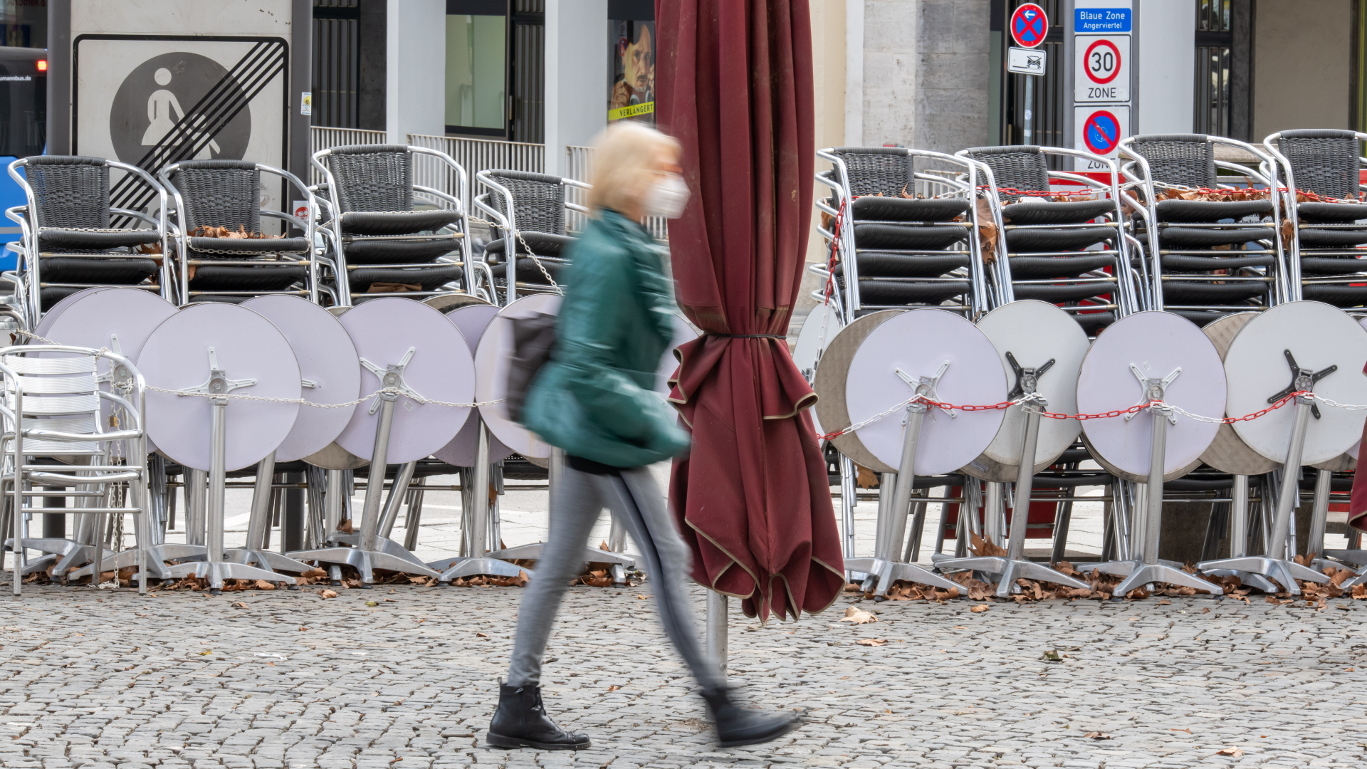 Eine Frau geht an zusammengestellten Tischen und Stühlen eines Cafés in der Innenstadt von München vorbei. 