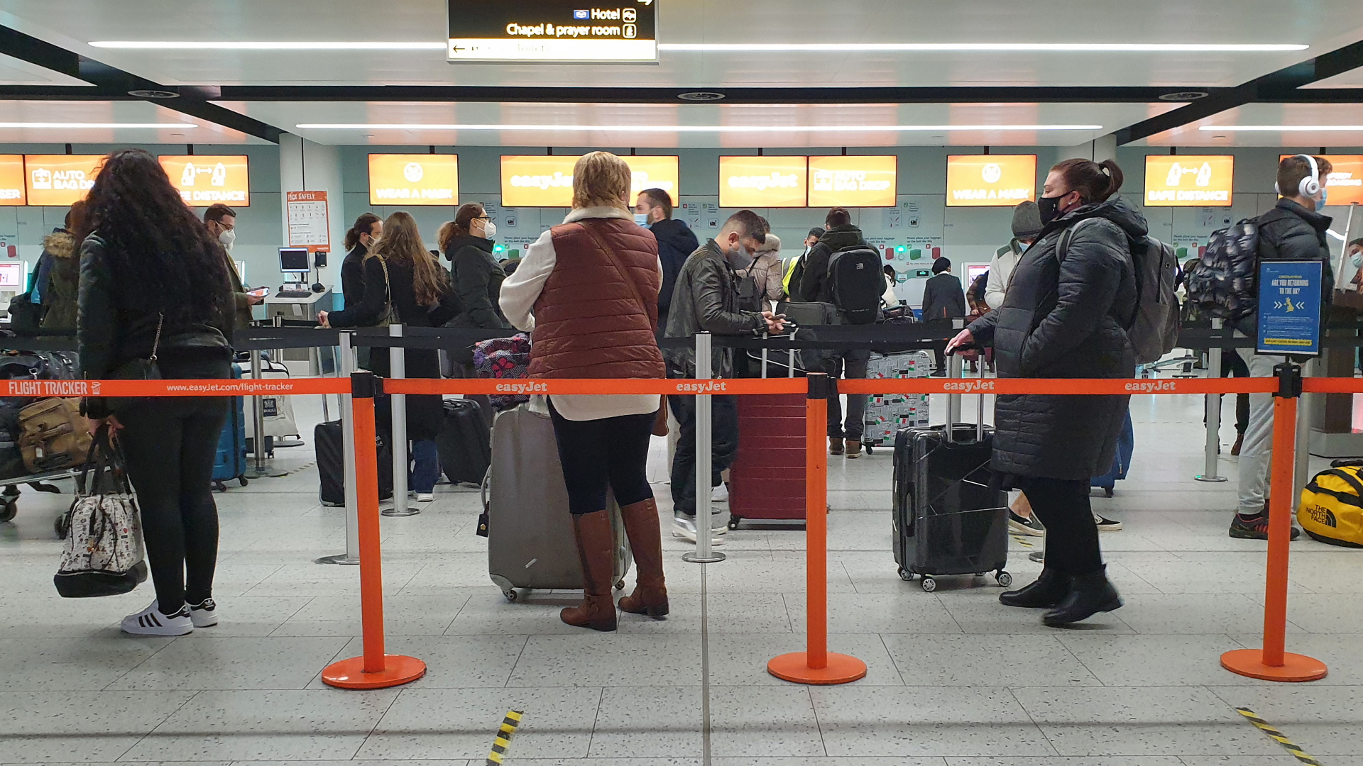 Passagiere stehen am Flughafen Gatwick in einer Schlange hinter einem Absperrband und warten.