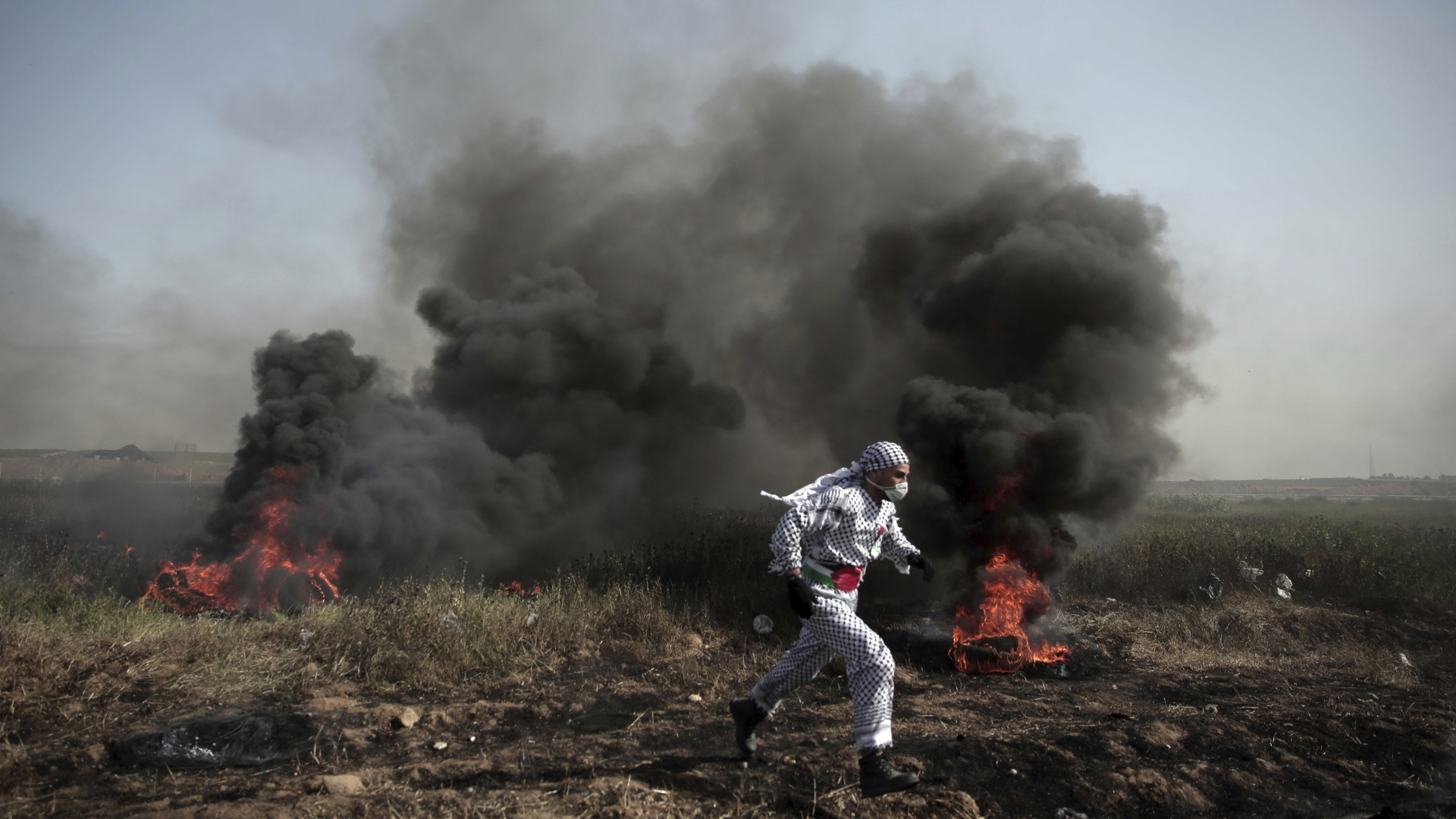 Ein Palästinenser voe brennenden Reifen bei Protesten im Gazastreifen. | AP